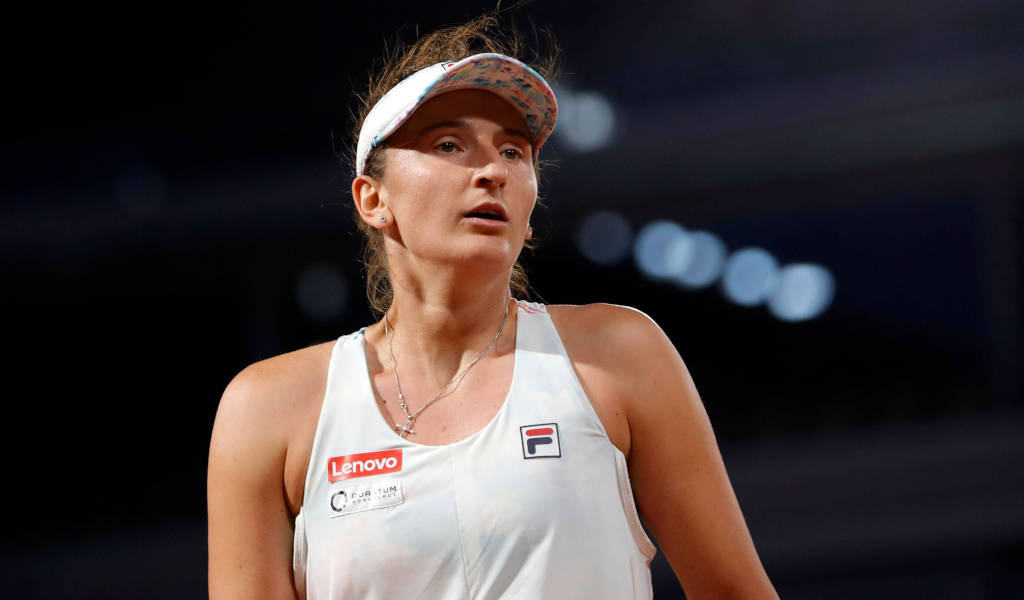 WTA總決賽網球選手伊琳娜-卡梅利婭·貝古 壁紙 — 一位專注的女網球運動員穿著白色運動裝備，在明亮的體育場燈光下於夜間比賽中向上看。