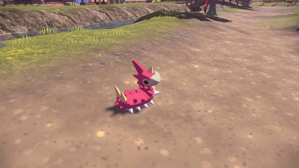 Wurmple在Pokémon Legends Arceus中 壁紙 — 一隻粉紅色、有尖刺、長著白色角和圓眼睛的寶可夢，在明亮的日光下，沿著一條泥路行走，旁邊是長滿草的河岸。