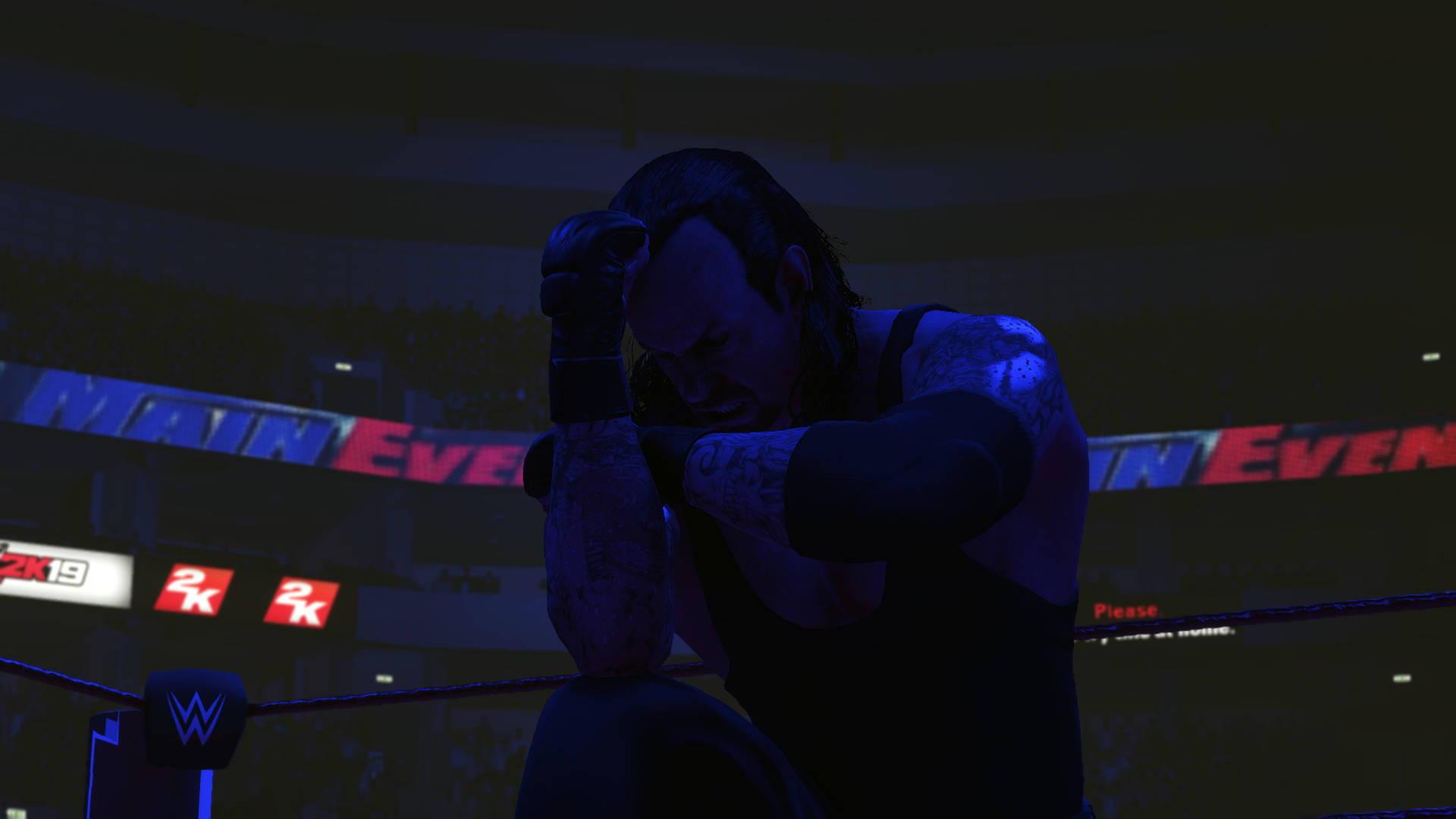 WWE 2K19 送葬者 壁紙 — 一名摔角手在黑暗的擂台上，在藍色場館燈光下痛苦地跪著，身後有『MAIN EVENT』的橫幅在發光。