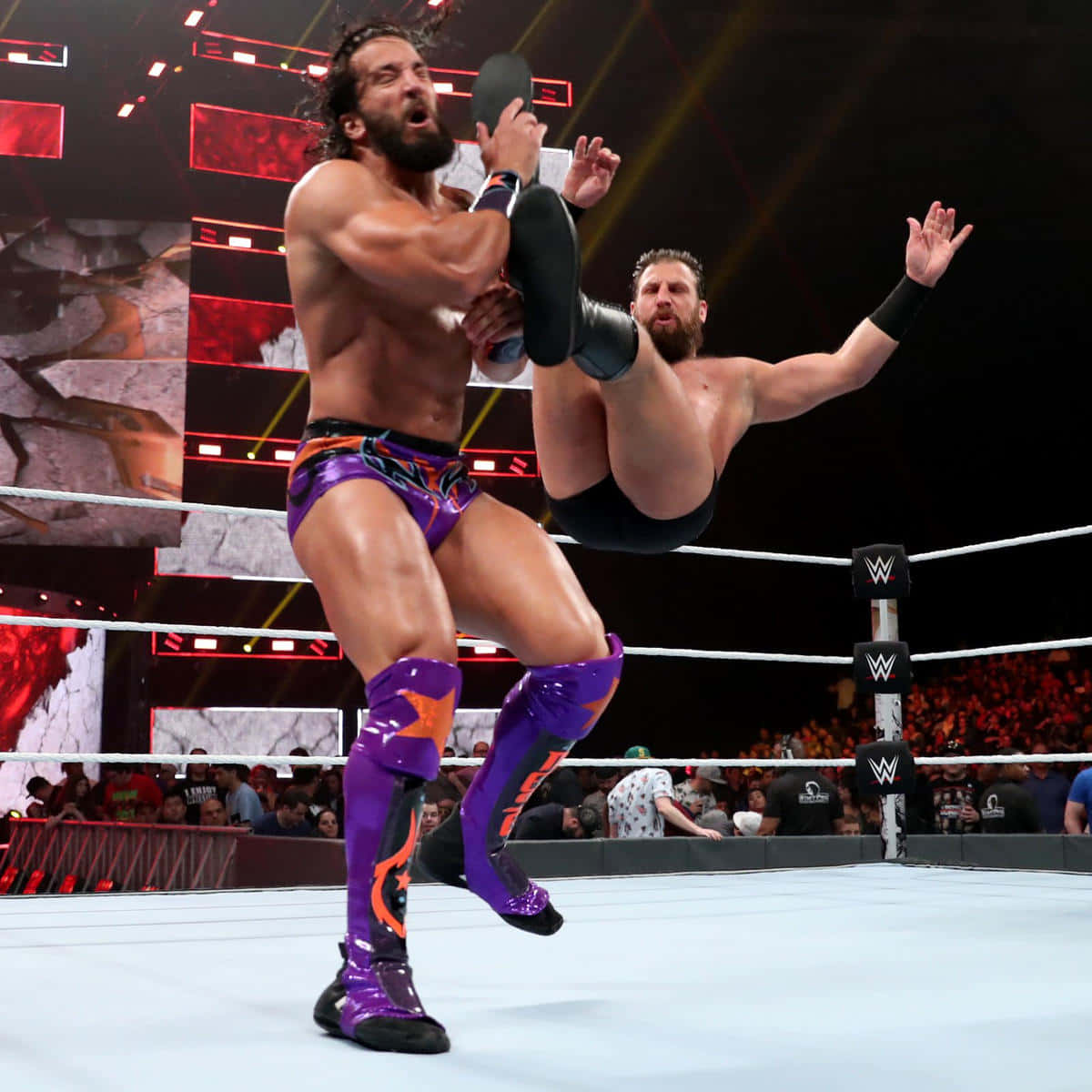 托尼·尼澤 WWE 職業摔角手 壁紙 — 一名穿著紫色裝備的摔角手在明亮的場館燈光下舉起對手，準備施展高衝擊力招式。