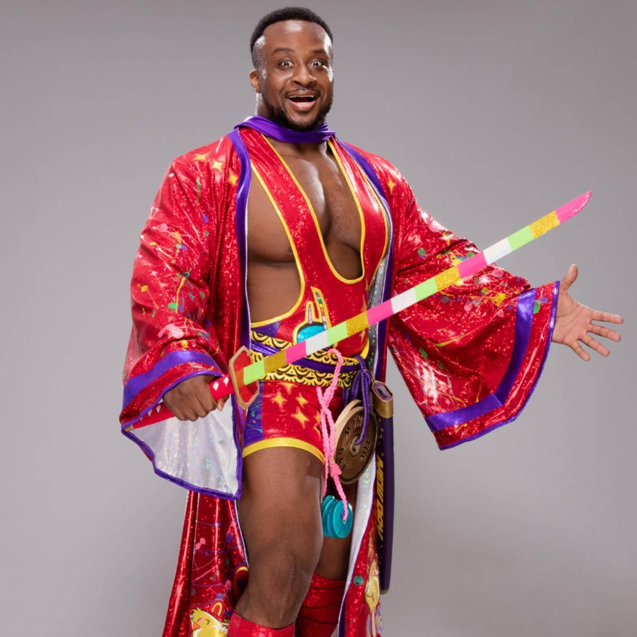 WWE Big E 的武士造型 壁紙 — 一名身穿搶眼紅紫色服裝、手持彩虹劍的摔角手，在純灰色背景前充滿活力地擺姿勢。