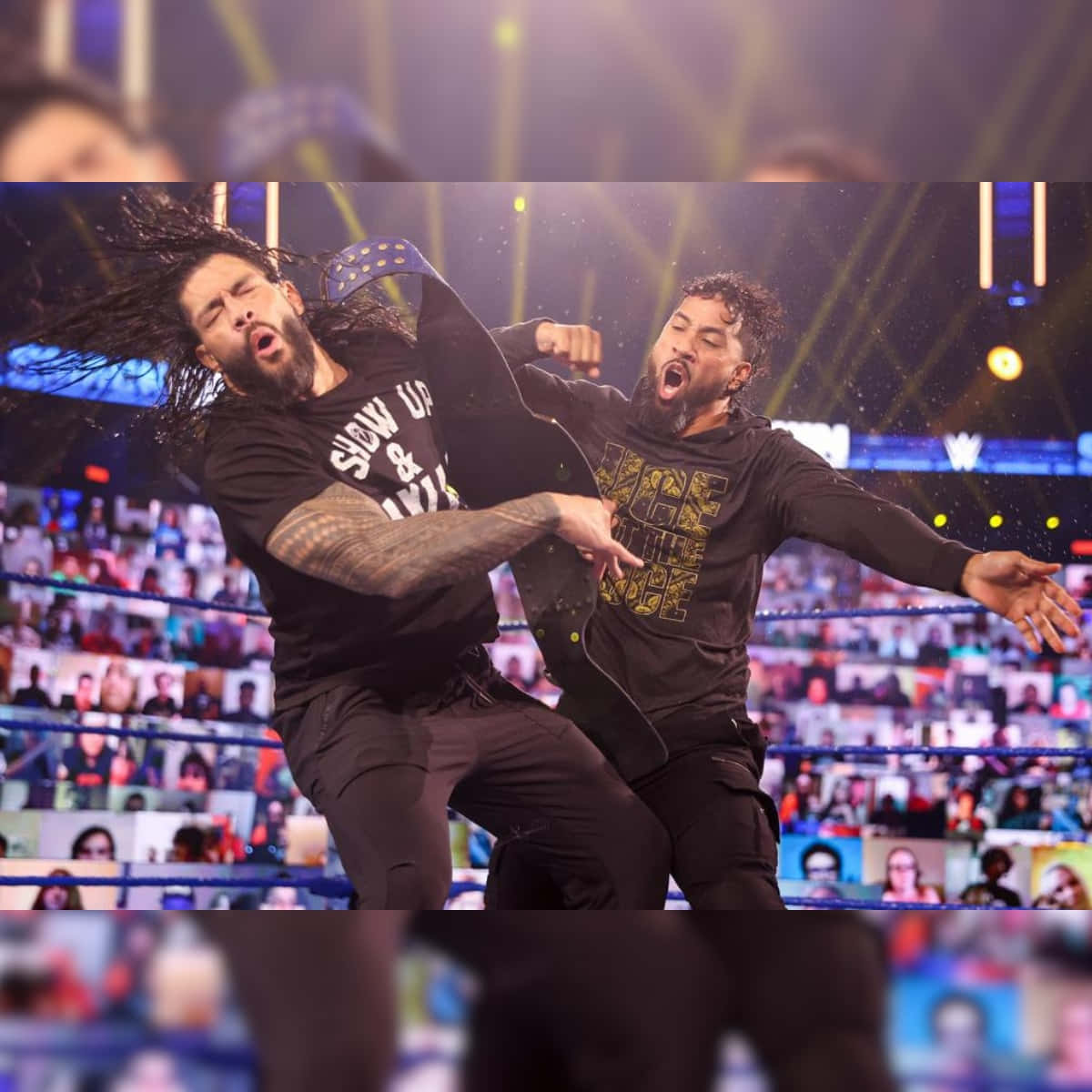 WWE Jey Uso 與 Roman Reigns 激烈對戰 壁紙 — 兩名摔角手在明亮的舞台燈光下於擂台上交鋒，繩索上有一群虛擬粉絲。