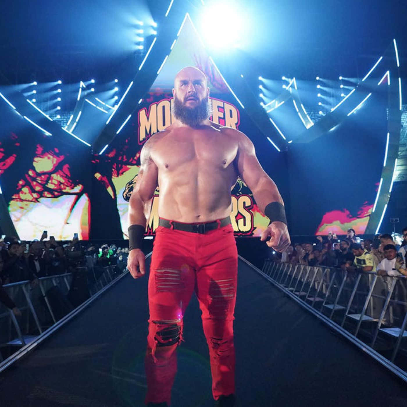美國職業摔角手布蘭恩·史勞曼 WWE Monday Night Raw驚喜回歸 壁紙 — 一位肌肉發達、留鬍子的摔角手穿著破爛的紅色褲子，在明亮的舞台燈光下沿著明亮的競技場坡道走向咆哮的粉絲。