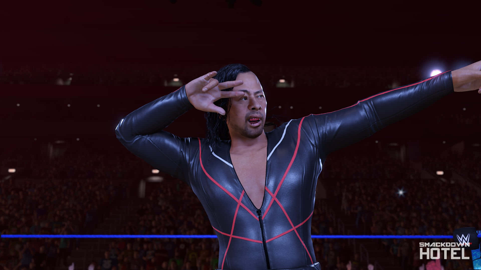 WWE遊戲中邑真輔慶祝舞蹈 壁紙 — 一名身穿黑紅戰衣的摔角手在明亮的聚光燈下，於座無虛席的場館中擺出戲劇性的姿勢。