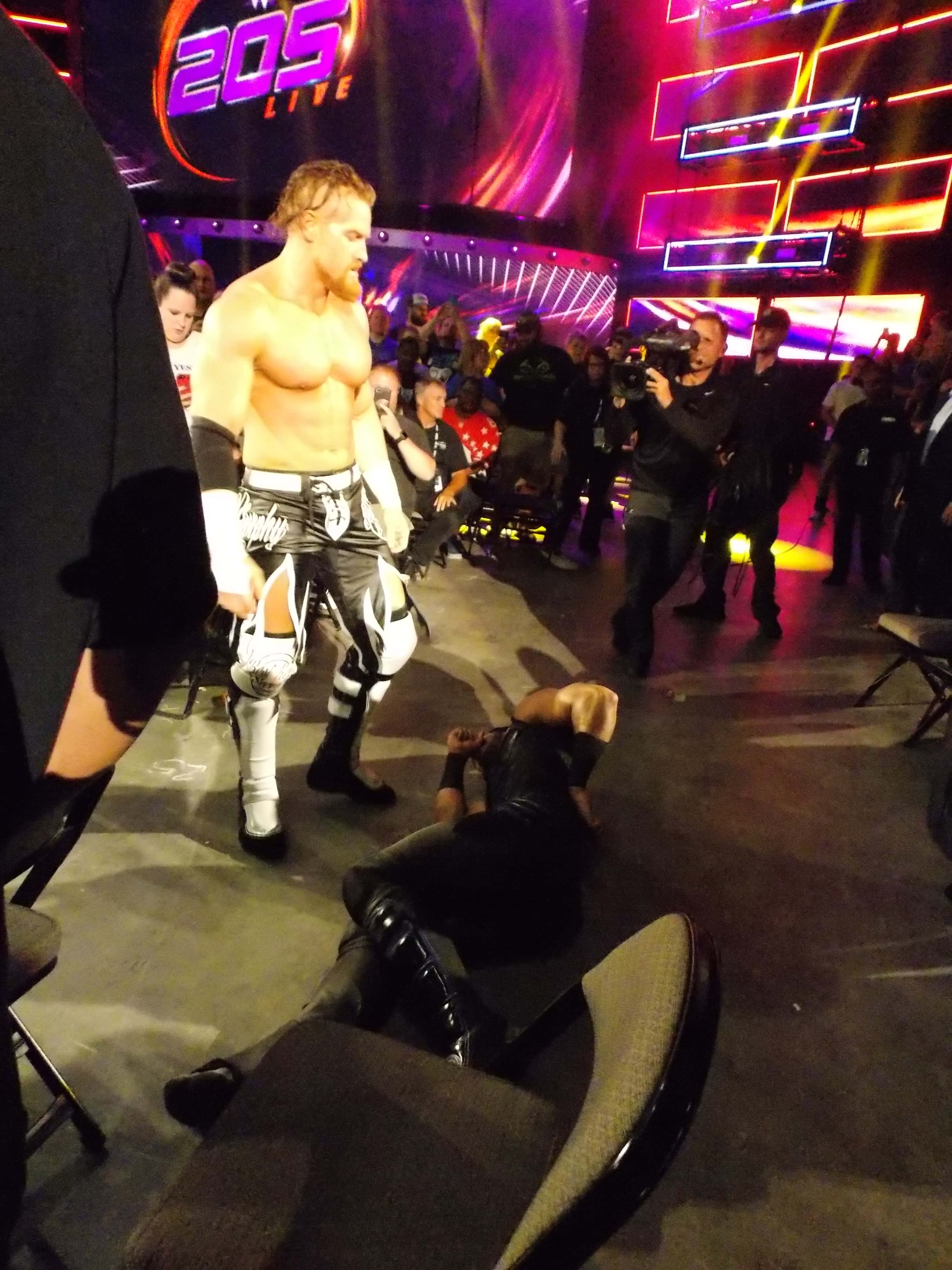 巴迪·墨菲對戰穆斯塔法·阿里 WWE SmackDown 壁紙 — 一名肌肉發達的摔角手身穿黑白裝備，在充滿活力的紫色和橙色燈光下，站在舞台上倒下的對手之上。
