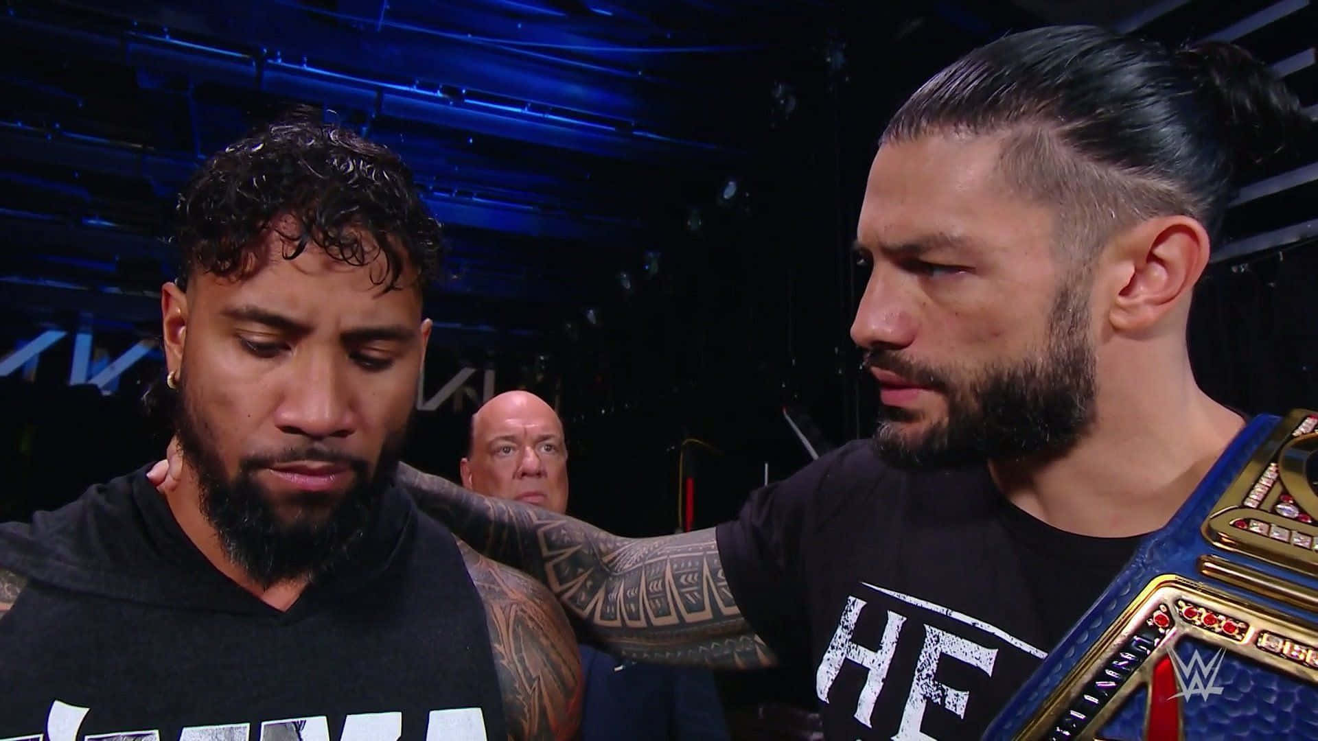 WWE Smackdown Jey Uso 與 Roman Reigns 壁紙 — 兩名摔角手在燈光昏暗的場地中對峙，一人手持冠軍腰帶，另一人神情沮喪。