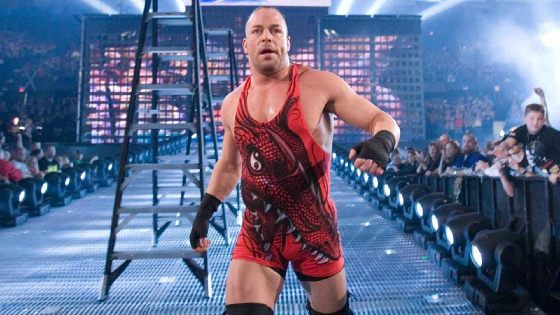 WWE 羅布·范·達姆登場照 壁紙 — 一位肌肉發達的摔角手穿著紅色龍主題緊身衣，自信地走下一條燈火通明的競技場坡道，旁邊放著一把梯子。