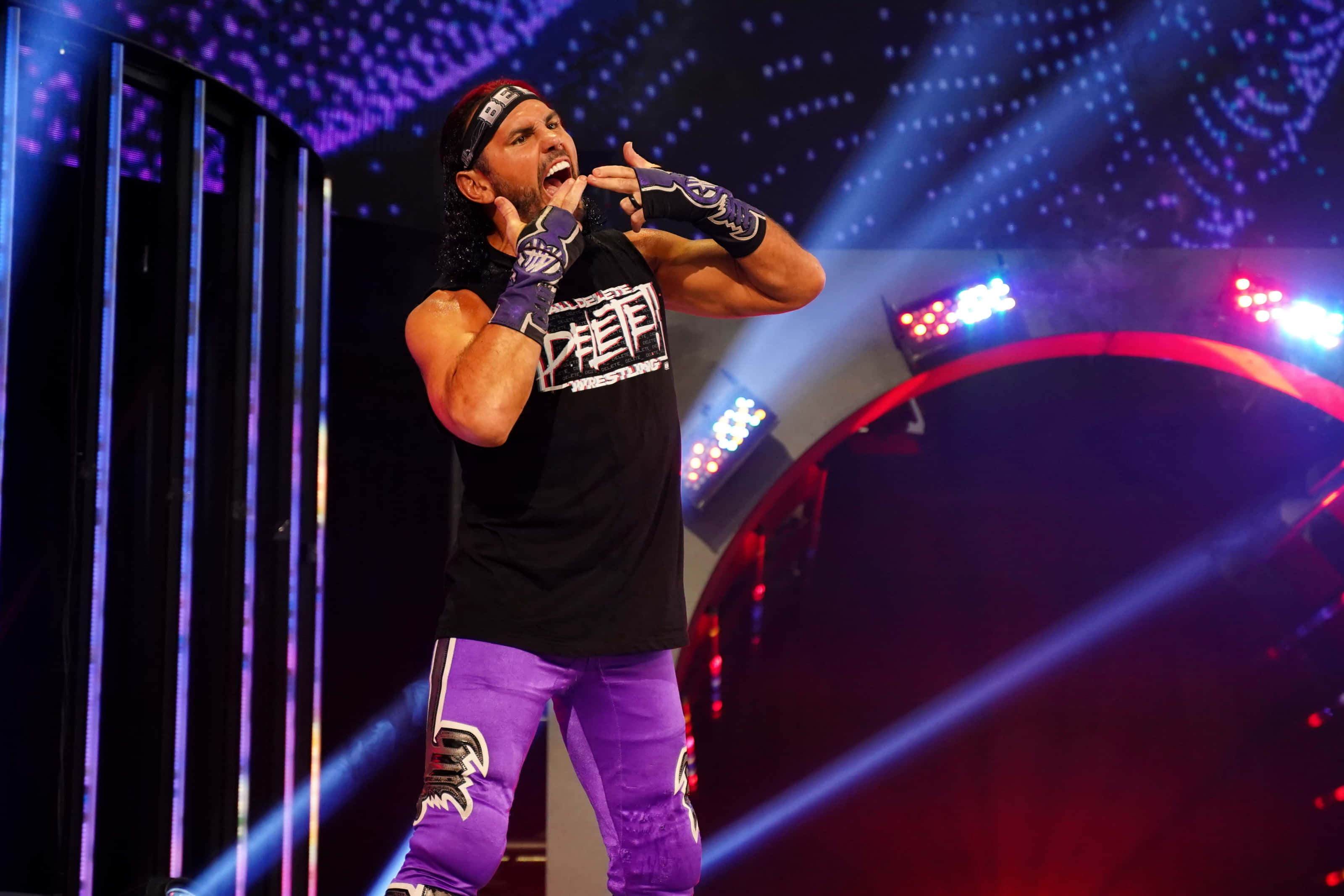 WWE 美國摔角手馬特·哈迪經典姿勢 壁紙 — 一位穿著紫色褲子和黑色襯衫的摔角手在充滿活力的舞台燈光、激光束和星空背景下熱情地尖叫。
