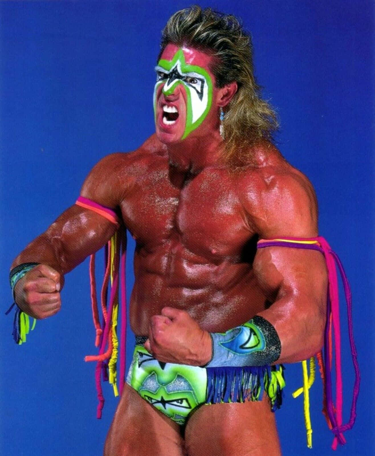WWE傳奇人物 Ultimate Warrior 身著經典霓虹服裝 壁紙 — 一位肌肉發達的摔角手，臉上塗著綠色和白色的顏料，在純藍色背景前咆哮。