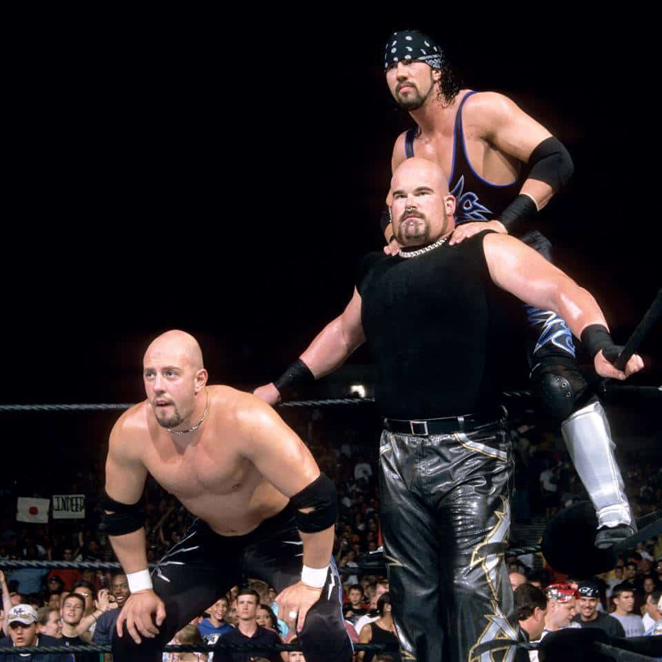 WWE傳奇人物賈斯汀·克瑞迪爾與 X-Pac 與 Albert 擊掌擂台壁紙 壁紙 — 三名肌肉發達的摔角手在擂台上，其中一人騎在另一人身上準備進行高衝擊力的動作。