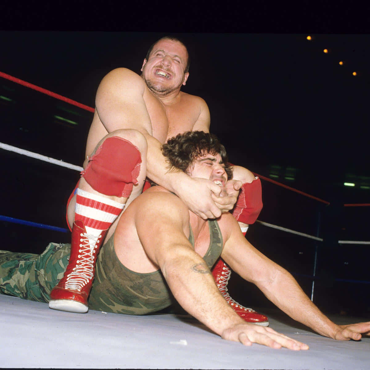 WWE名人堂成員尼古拉·沃科夫比賽瞬間 壁紙 — 兩名肌肉發達的摔角手在擂台上激烈纏鬥，一人穿著紅色靴子和迷彩褲，另一人穿著綠色短褲。