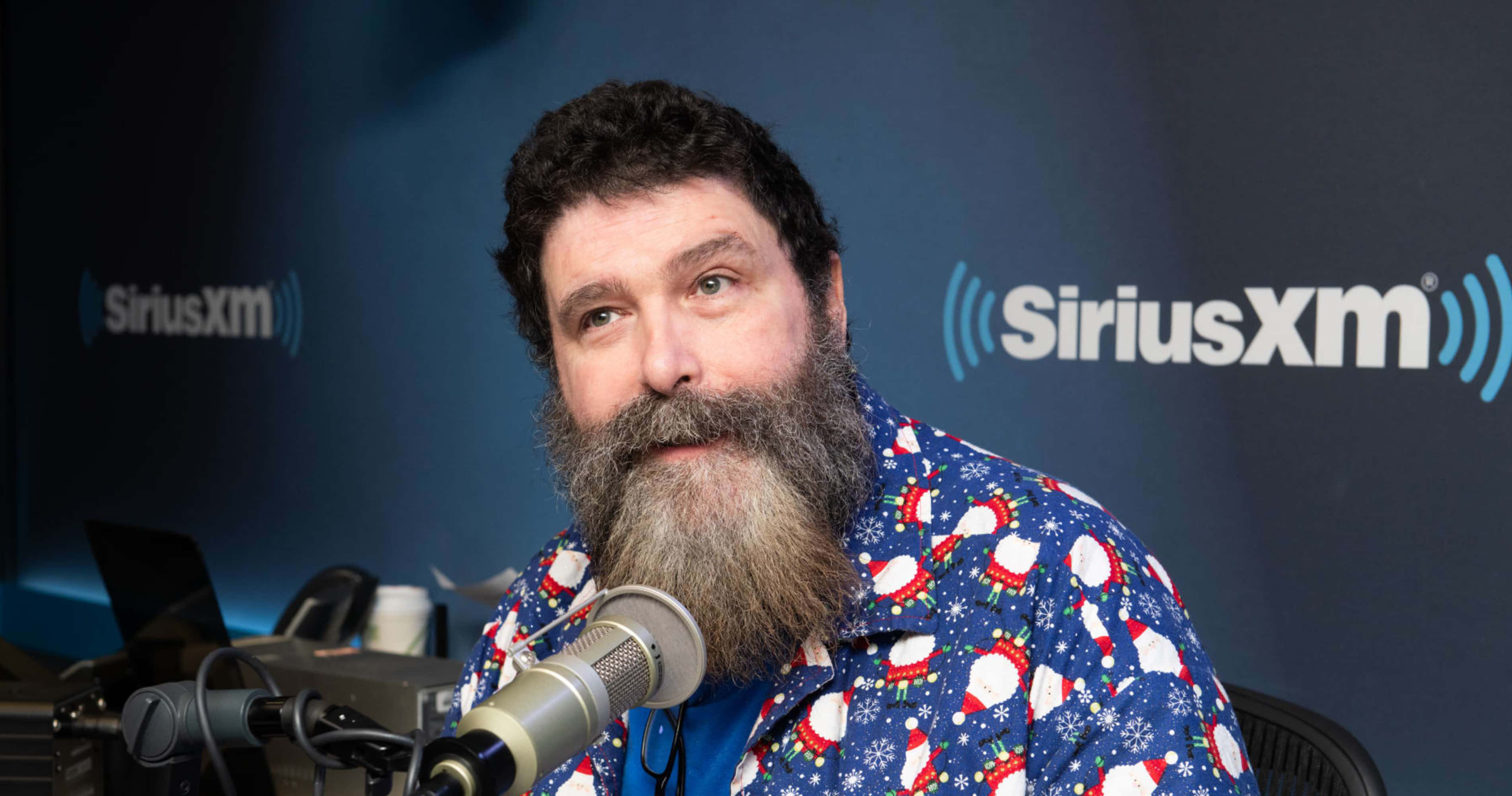 WWE名人堂成員米克·福萊造訪SiriusXM錄影室 壁紙 — 一位留鬍鬚的男子穿著節日聖誕主題襯衫，在SiriusXM錄音室對著麥克風說話。