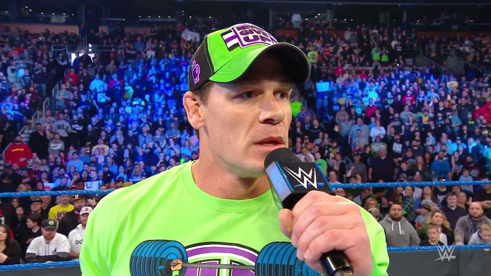 John Cena 桌布 壁紙 — WWE摔角手John Cena身穿鮮綠色裝備，在摔角場內對著麥克風說話，面前是歡呼的人群。
