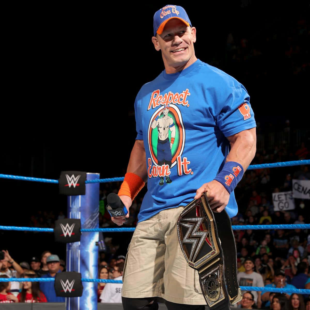 John Cena 桌布 壁紙 — WWE摔角手約翰·辛納在摔角擂台上自信微笑，手持冠軍腰帶和麥克風。