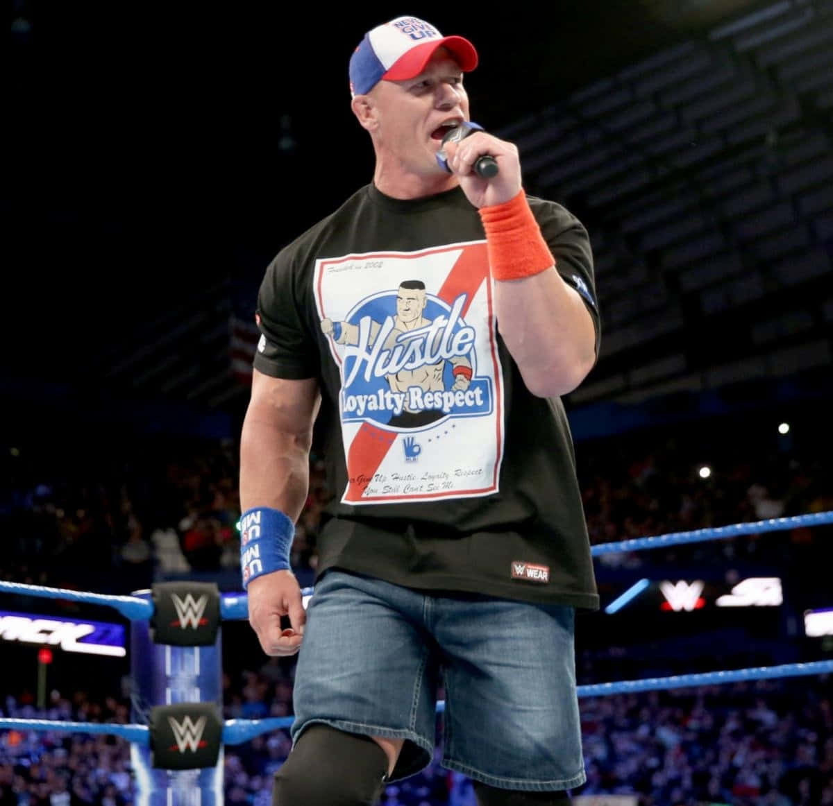 John Cena 桌布 壁紙 — WWE摔角手約翰·辛納站在擂台上手持麥克風，身穿「Hustle Loyalty Respect」T恤和愛國帽子。