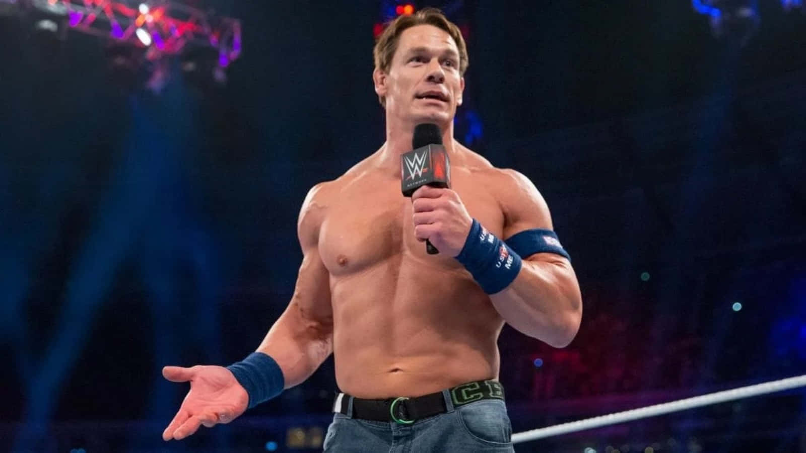 John Cena 桌布 壁紙 — WWE摔角手約翰·辛納赤裸上身站在擂台上，在明亮的舞台燈光下手持麥克風。