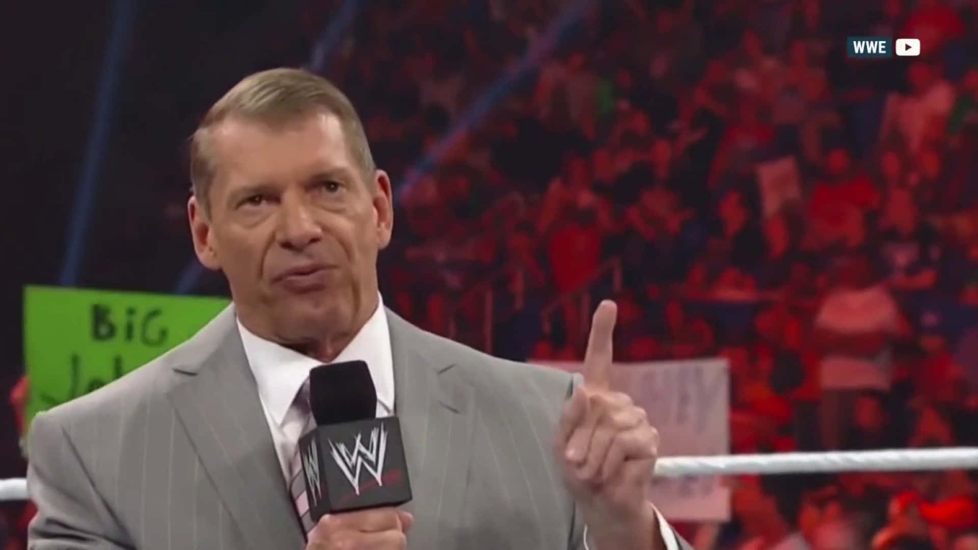 WWE 評述員 Vince McMahon 在摔角擂台上向上指，周圍有歡呼的人群。