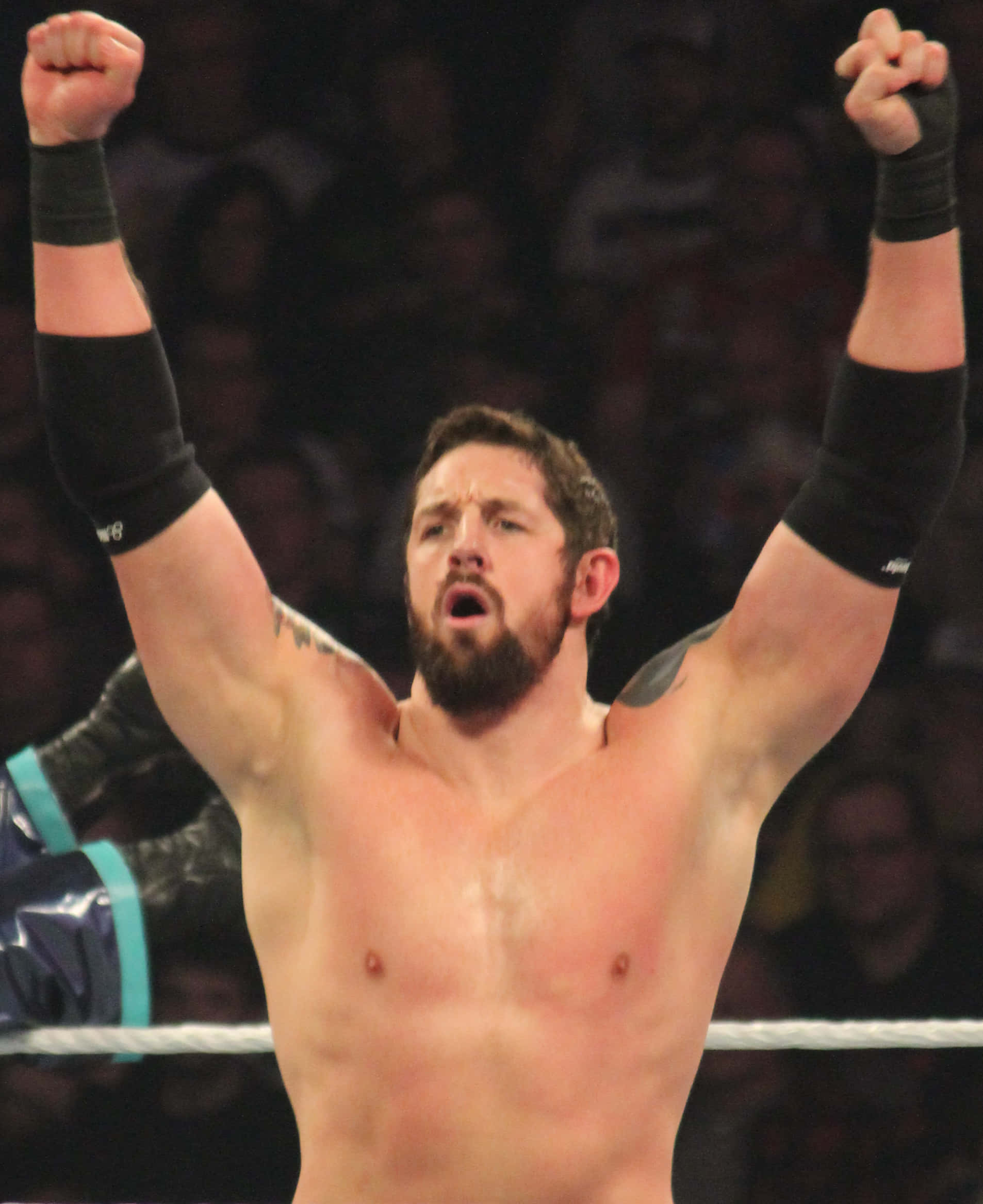 WWE明星韋德·巴雷特勝利慶祝 壁紙 — 一位肌肉發達、留鬍子的摔角手在擂台內高舉雙拳慶祝勝利，身後是模糊的人群。