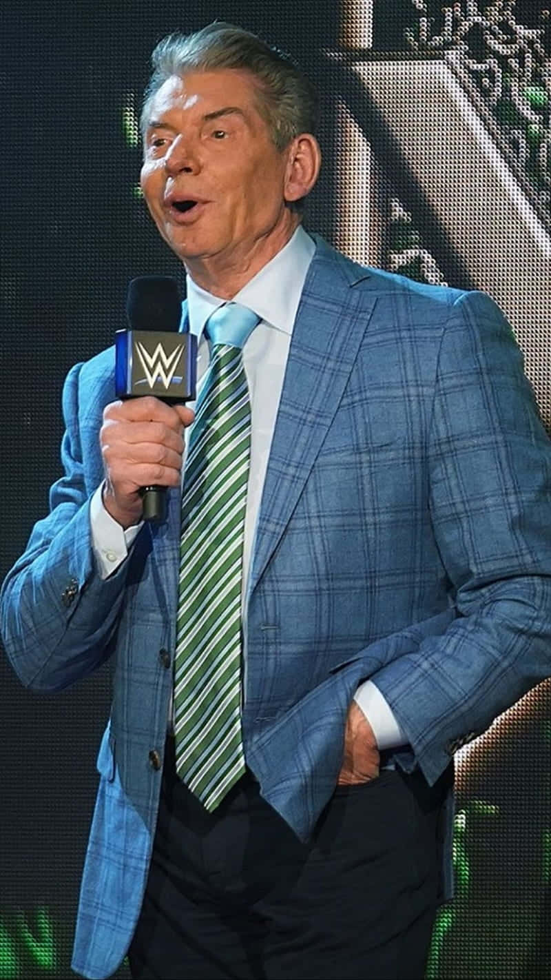 身穿藍色格紋西裝的WWE主持人拿著麥克風在舞台上
