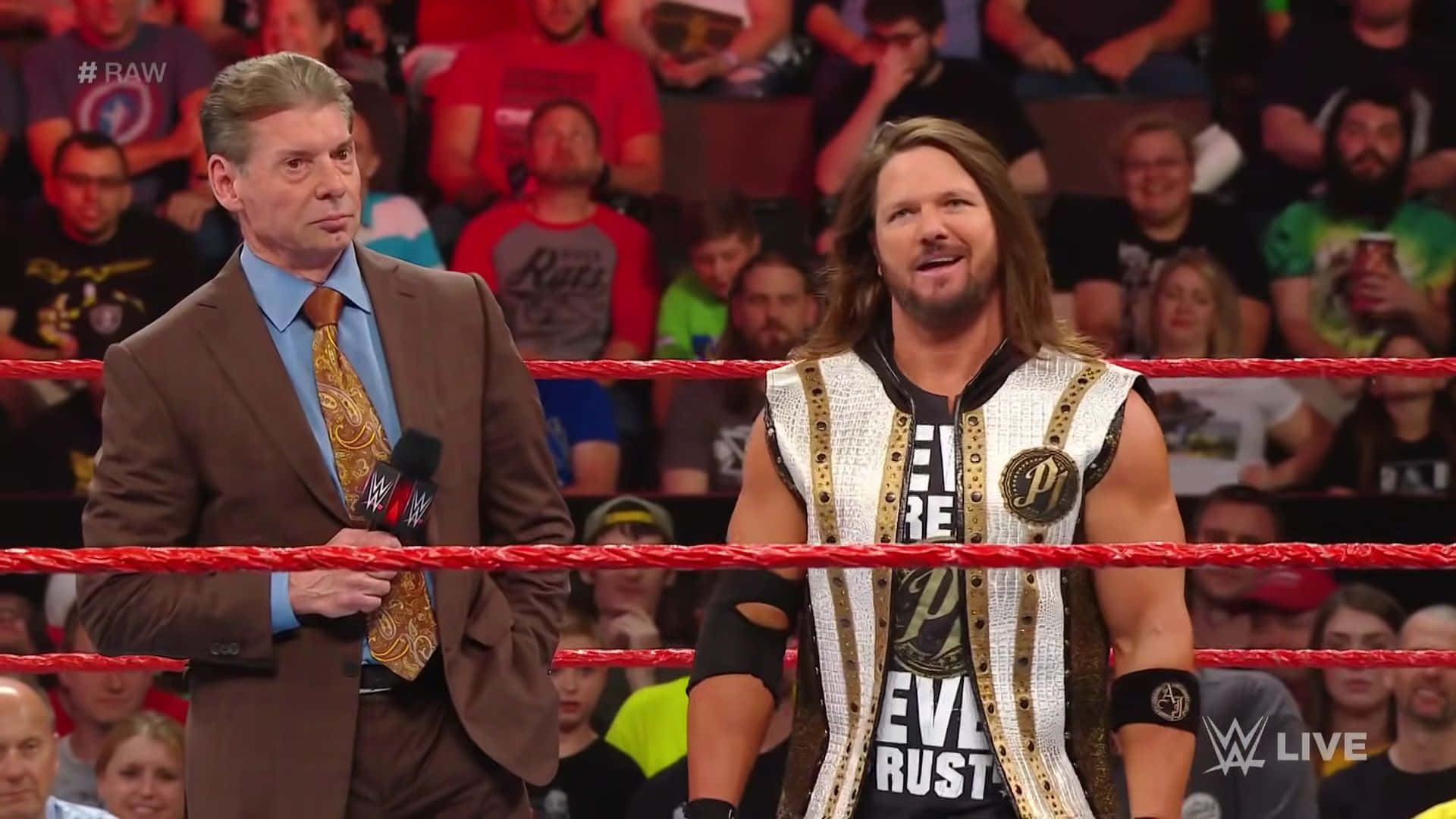 WWE 旁述員和摔角手在擂台上，紅色繩索後面有歡呼的人群。