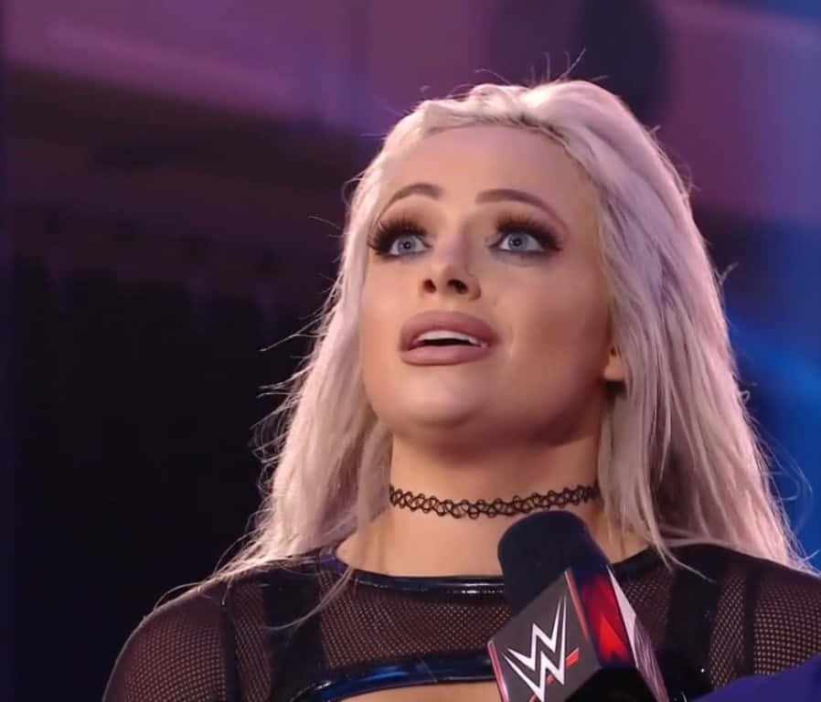 WWE摔角手在紫色燈光下在舞台上對著麥克風說話。