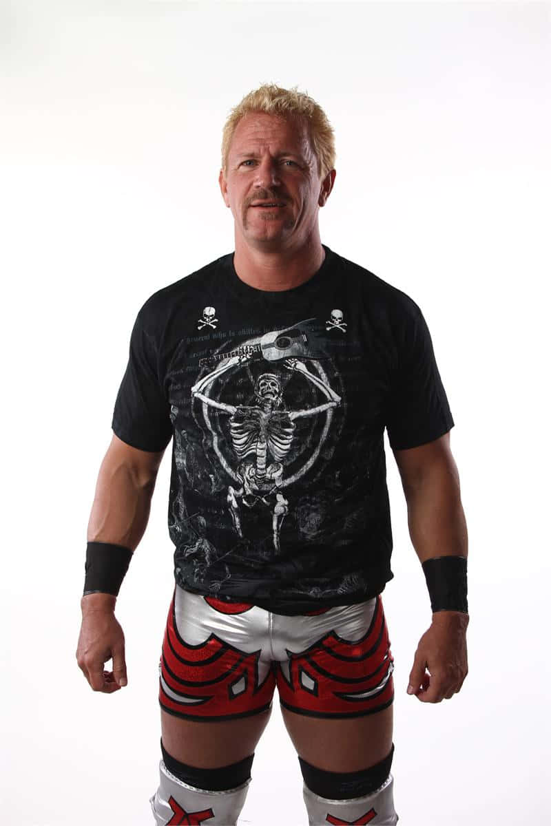 WWE超級巨星傑夫·賈雷特身穿經典服裝 壁紙 — 一位肌肉發達、金髮的摔角手自信地穿著紅色和銀色短褲及黑色骷髏圖案T恤，站在純白色背景前。