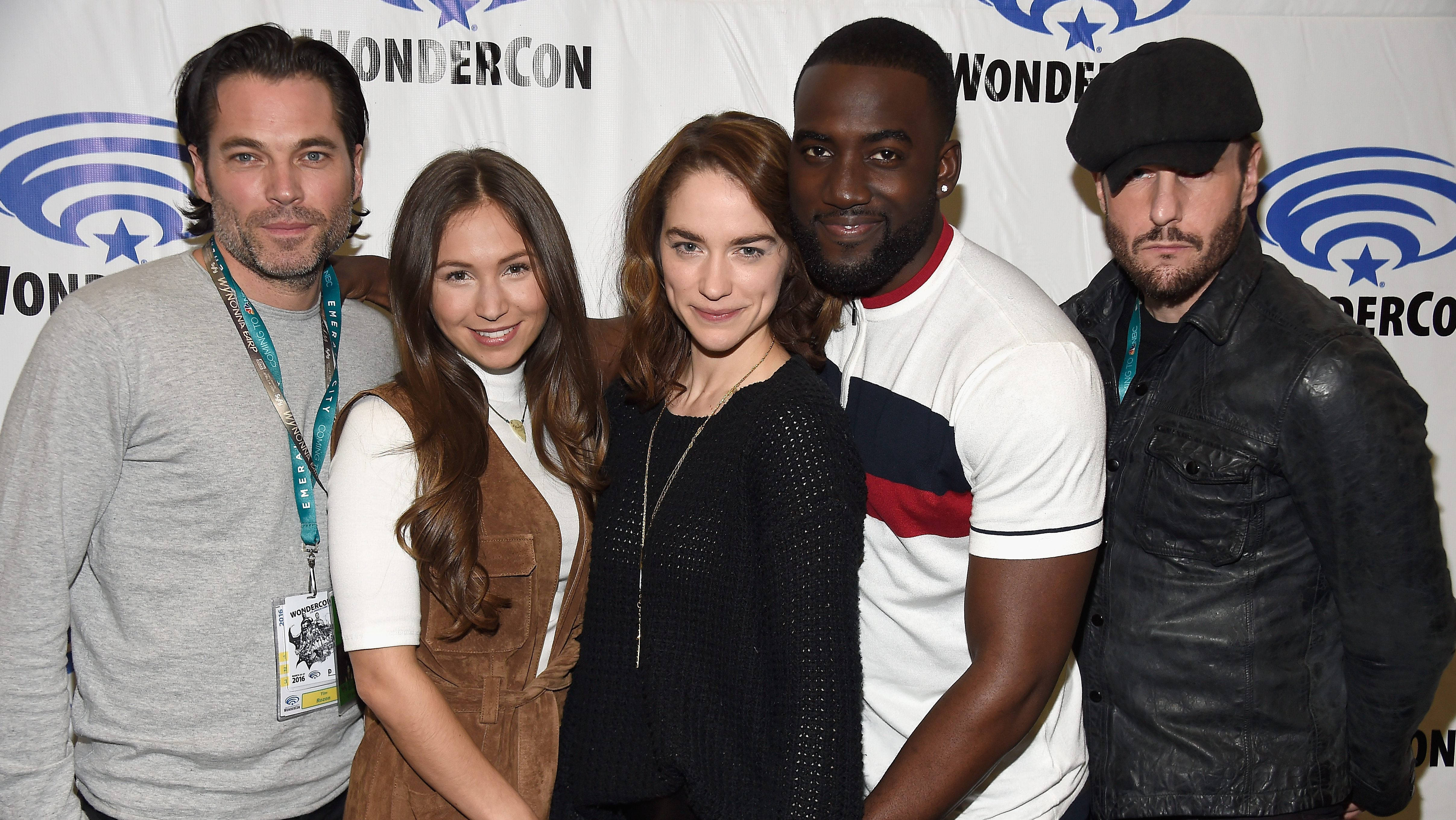Wynonna Earp 角色群 壁紙 — 五位演員在WonderCon座談會上一起擺姿勢，背景有品牌標誌並佩戴證件掛繩。