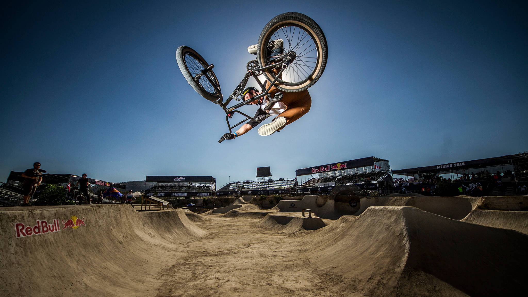 X Games BMX騎手躍起 壁紙 — 一名BMX車手在泥地賽道上空飛翔，在晴朗藍天下於Red Bull活動中表演極限技巧。