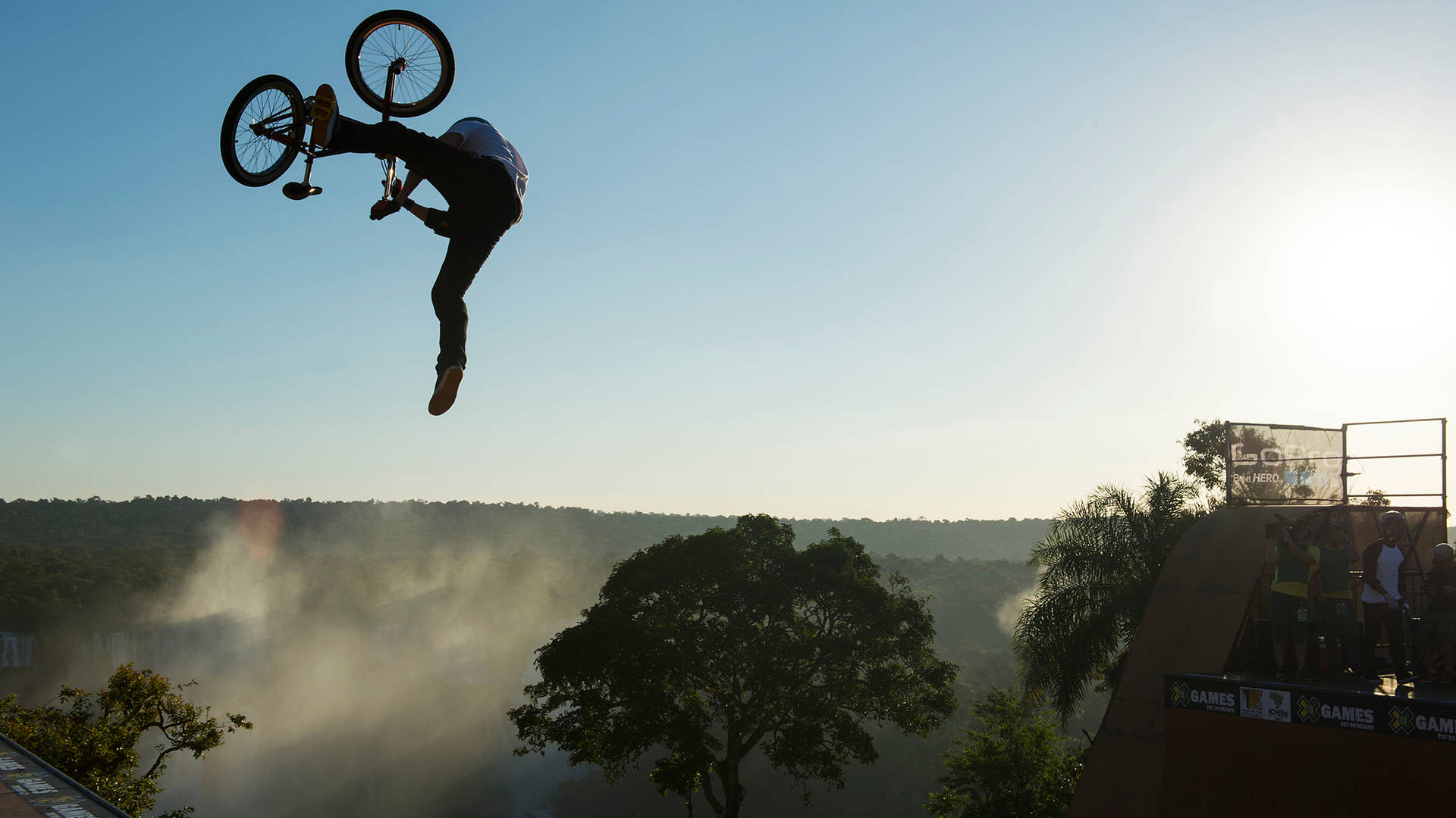 BMX車手在日出時於樹木繁茂的山谷上空進行高跳躍。
