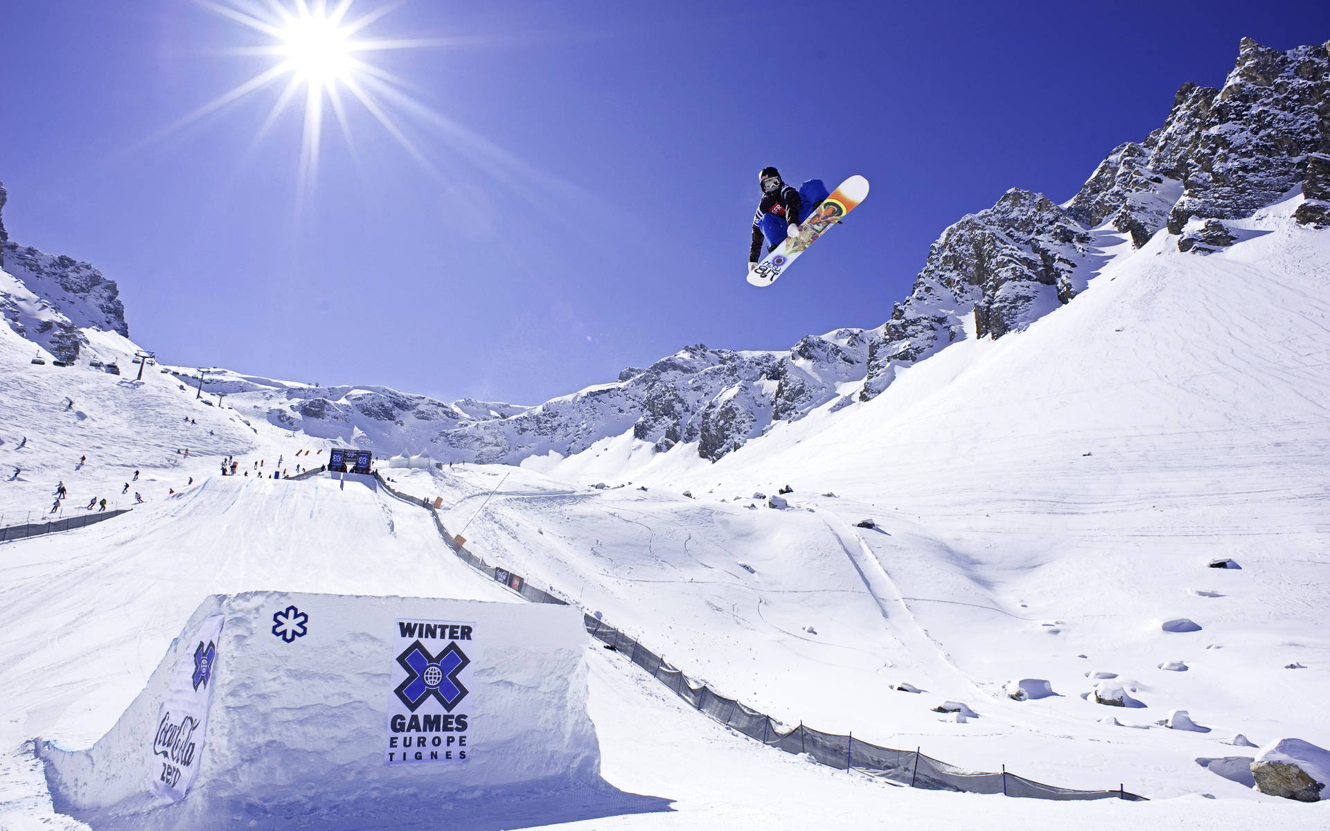 X Games 歐洲 Travis Rice 壁紙 — 在歐洲冬季極限運動會上，一名滑雪板運動員在熾熱的陽光下，飛越雪坡。