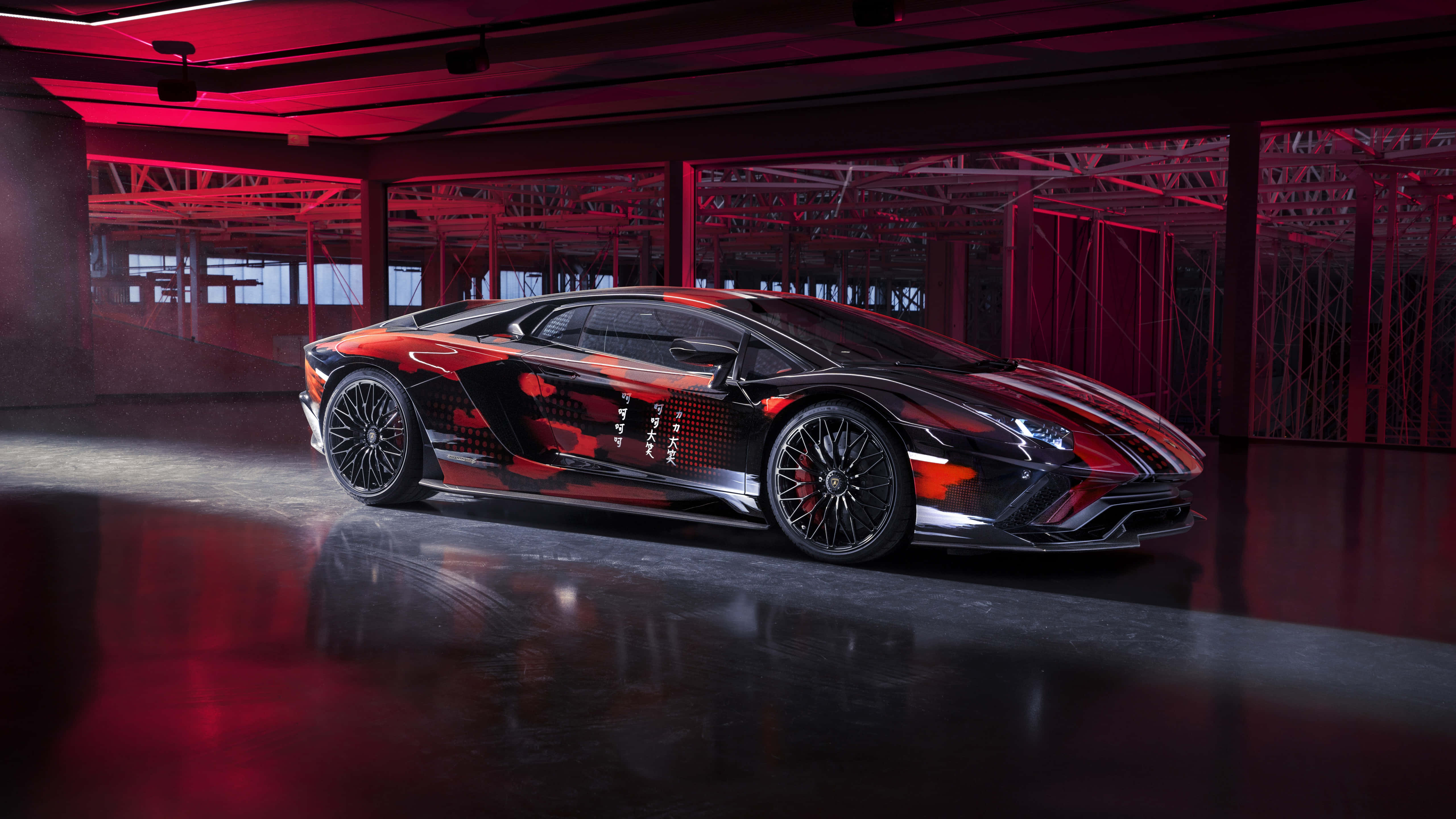 山本耀司 x Lamborghini 合作款跑車 壁紙 — 一部時尚的黑紅配色林寶堅尼Aventador，帶有日文字元，在現代工業車庫中於戲劇性的紅色燈光下展示。