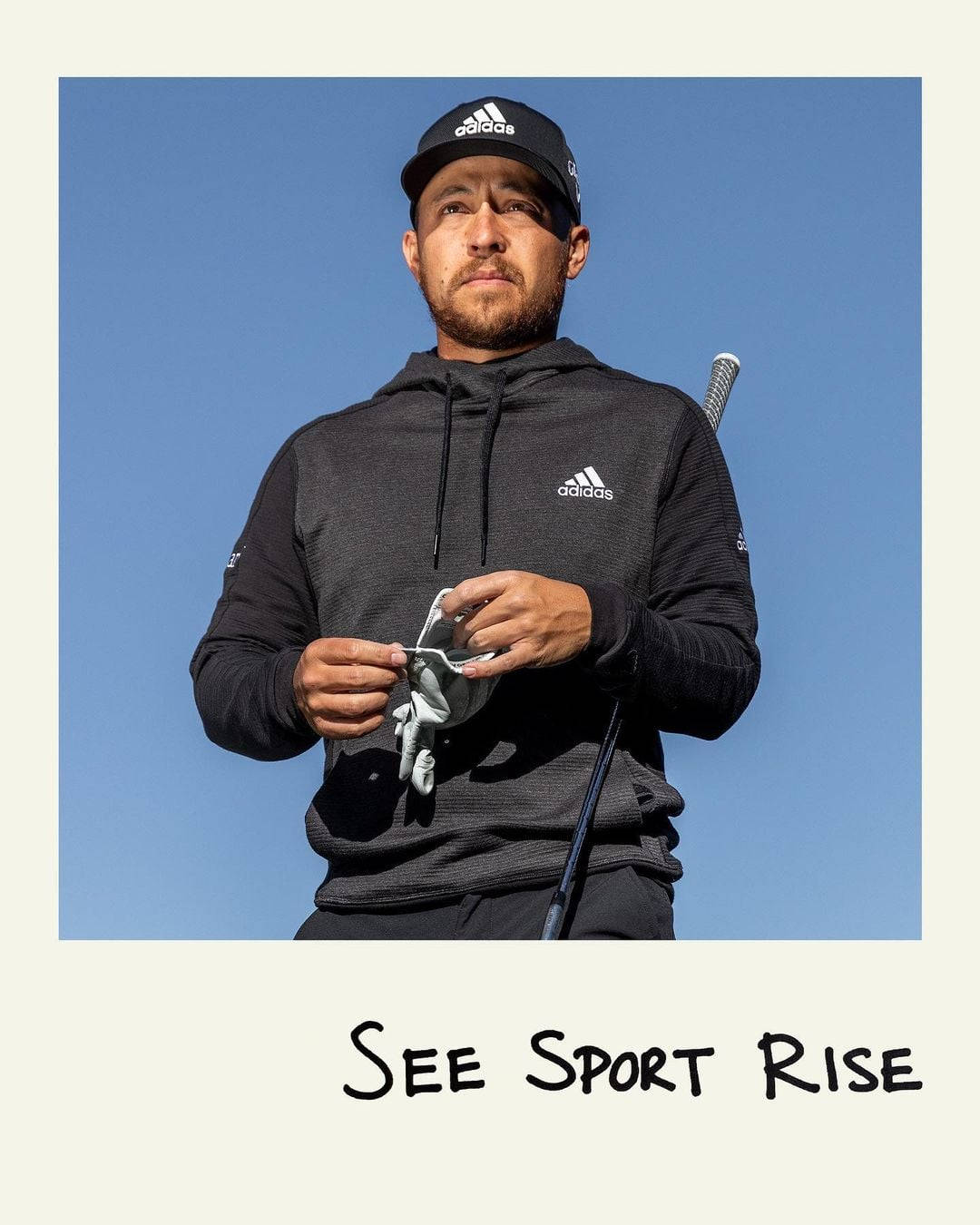 Xander Schauffele 身穿Adidas黑色外套與帽子，藍色背景拍攝 壁紙 — 一位專注的高爾夫球手穿著黑色adidas裝備，在清澈的藍天下拿著手套。