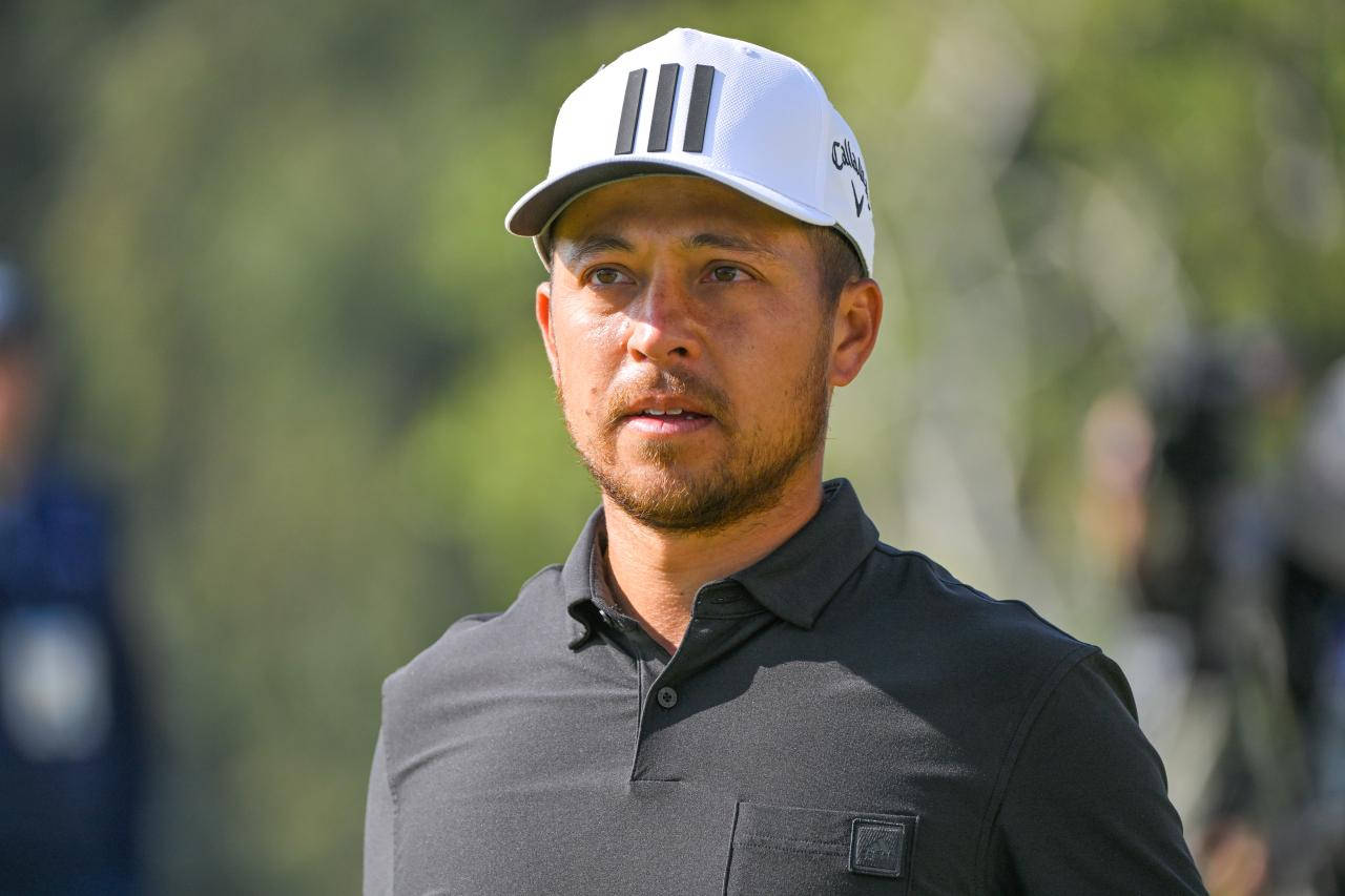 Xander Schauffele 半身肖像 壁紙 — 一位專注的高爾夫球手，戴著白色帽子，穿著深色Polo衫，站在模糊的綠色背景前。