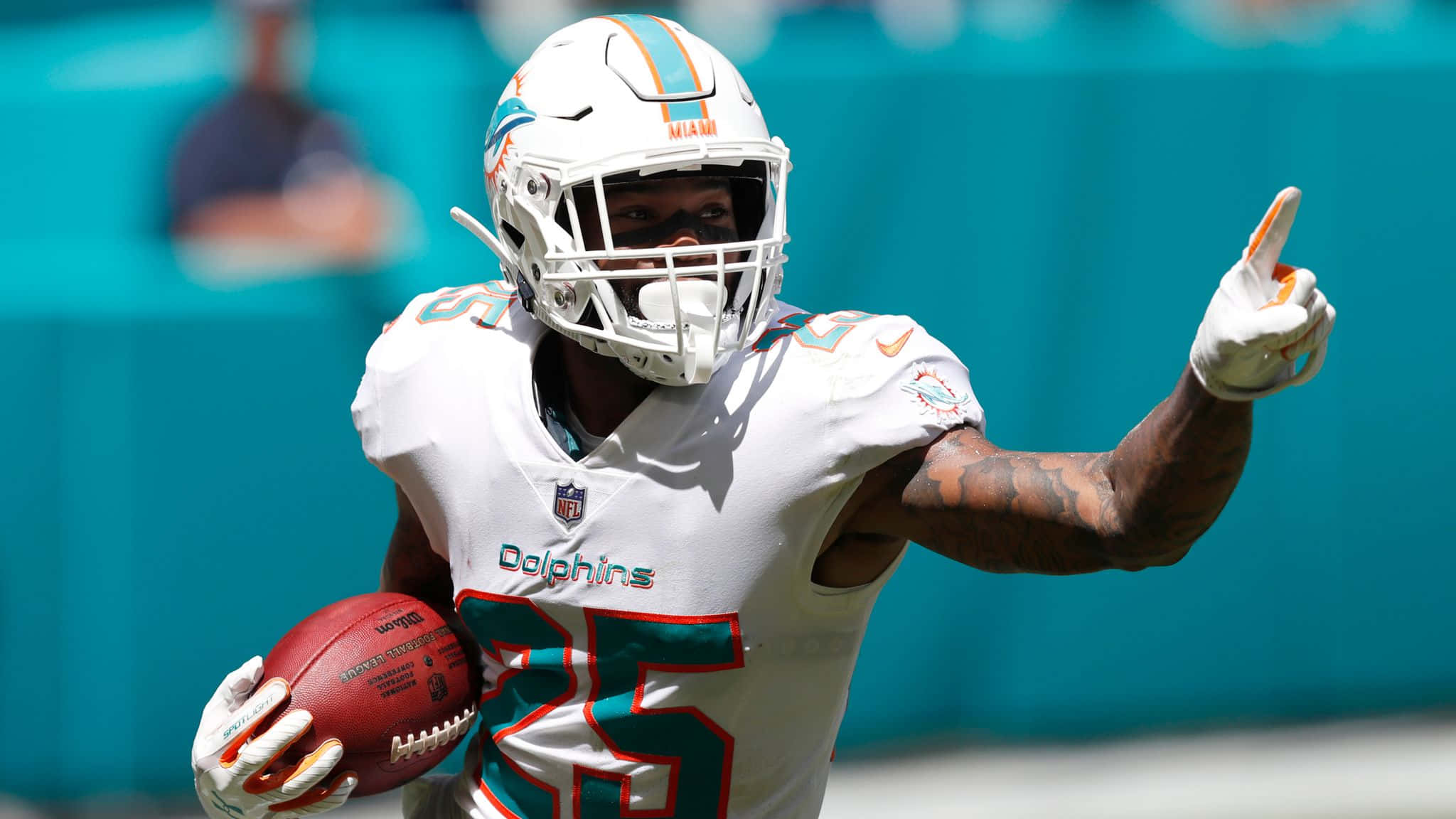 Xavien Howard 賽場即景 壁紙 — 邁阿密海豚隊美式足球員25號在明亮日光下抱著球以達陣手勢慶祝。