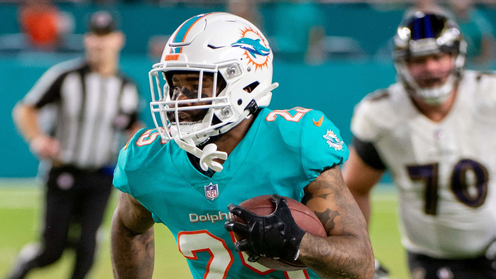 Xavien Howard 賽事動作瞬間 壁紙 — 一名穿著青綠色球衣的邁阿密海豚隊美式足球員在比賽中帶球奔跑，背景有裁判和對手。