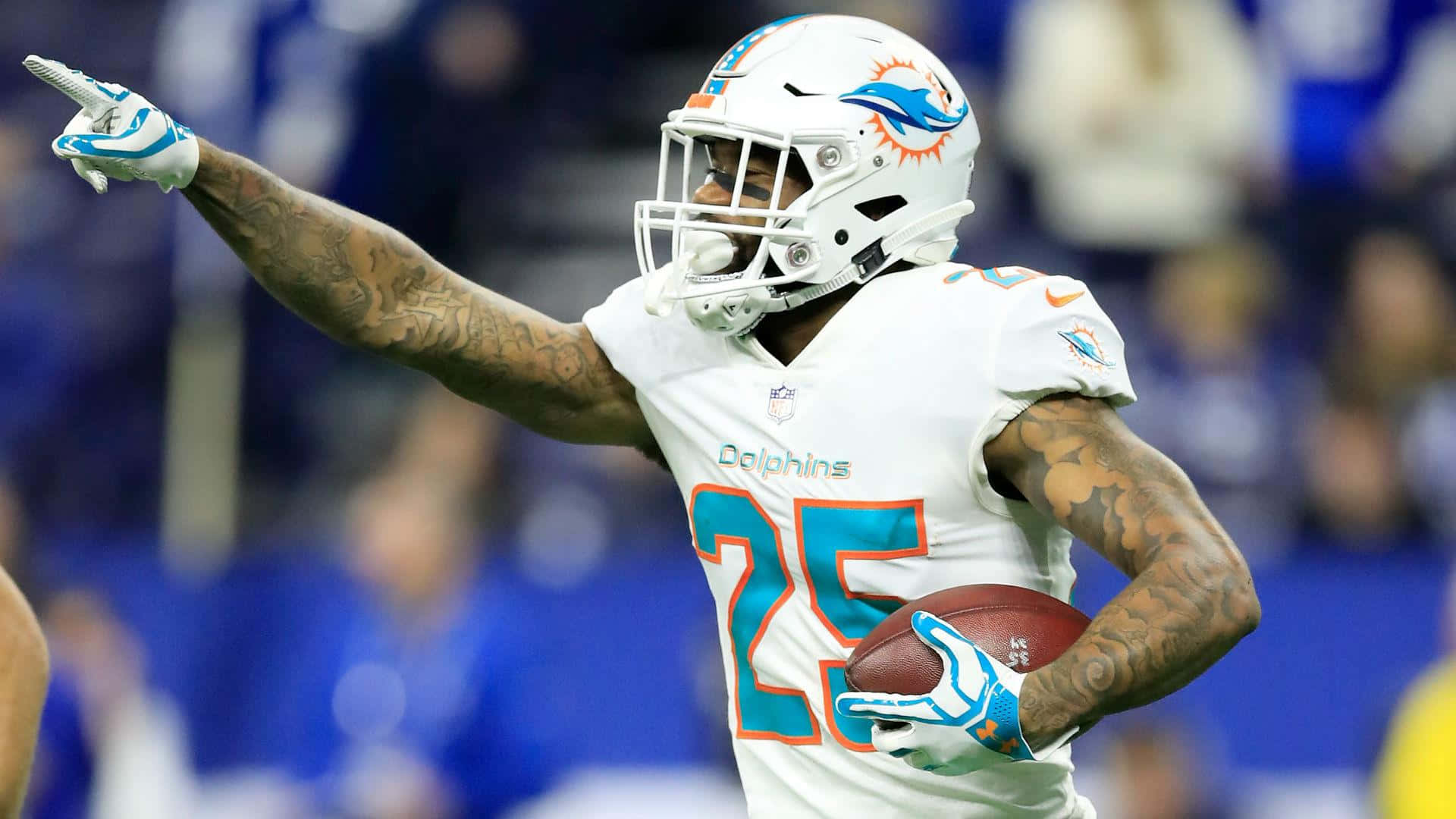 Xavien Howard 賽場即興照 壁紙 — 一位身穿白色25號球衣的邁阿密海豚隊美式足球員，拿著足球指向人群慶祝。