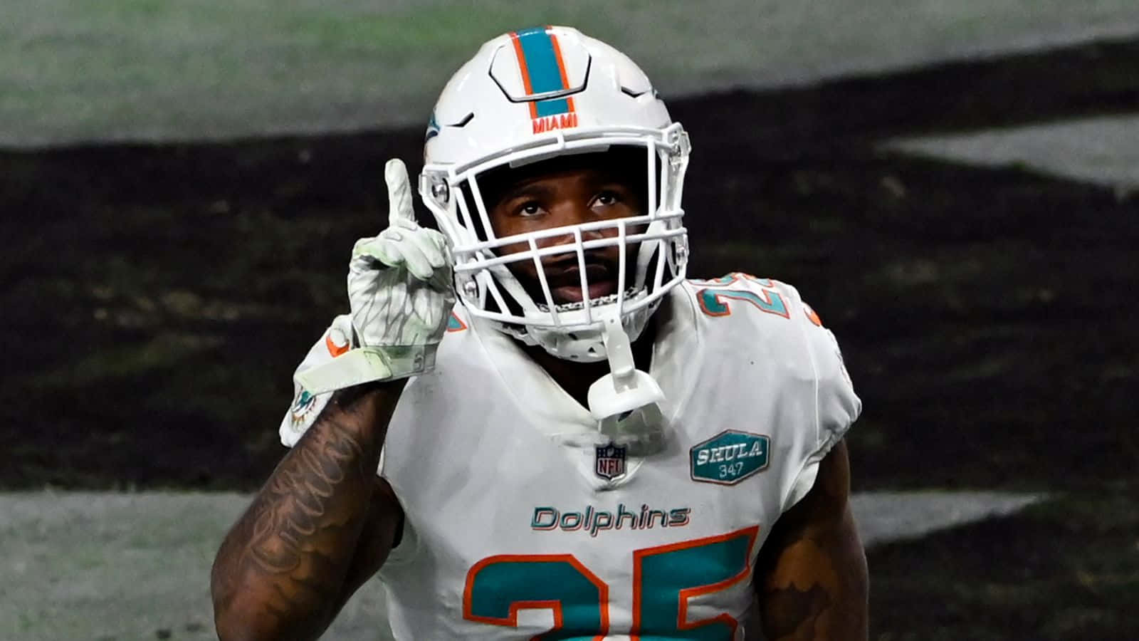 Xavien Howard 黑底編輯照 壁紙 — 邁阿密海豚隊美式足球員25號在明亮燈光下的體育場舉起食指慶祝。