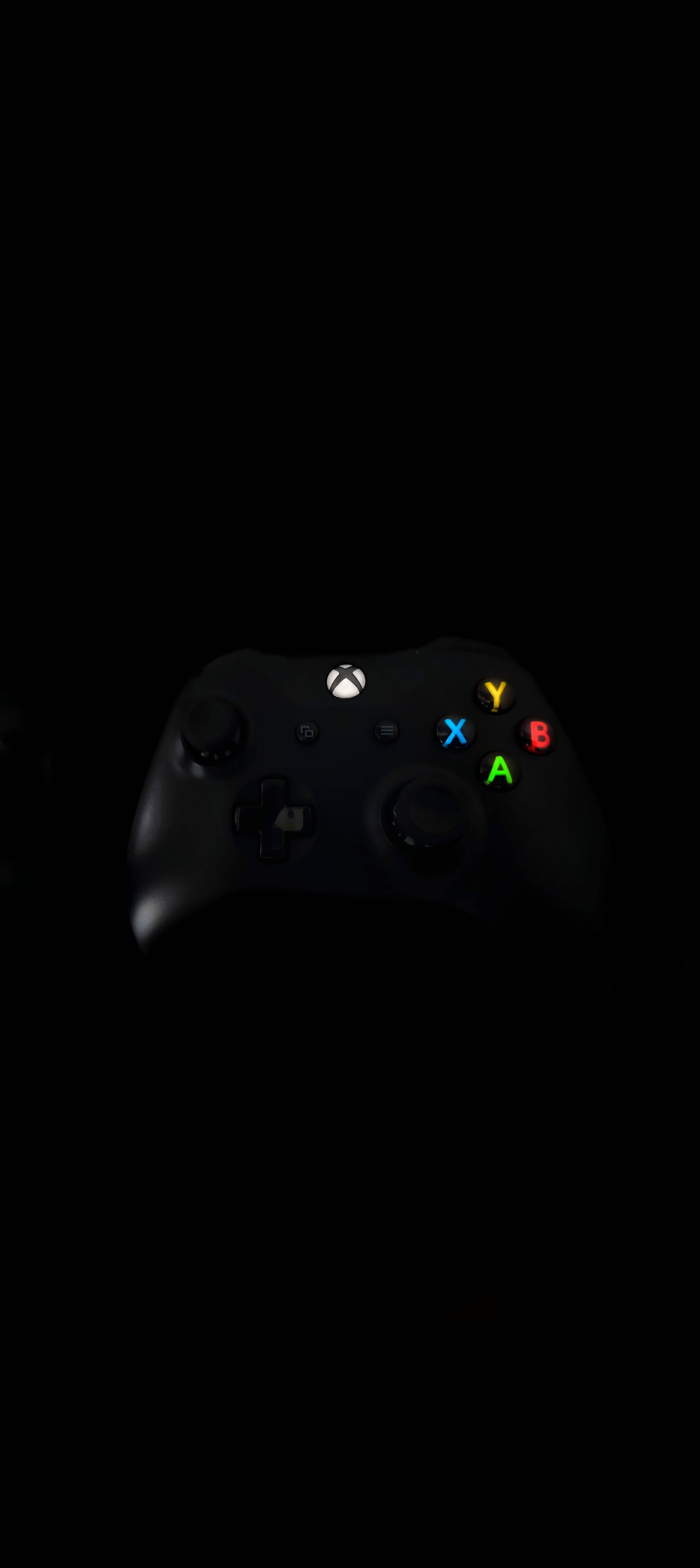 黑色Xbox手掣 8K 手機 壁紙 — 一個黑色Xbox手掣在漆黑背景上發出彩色按鈕的光芒。
