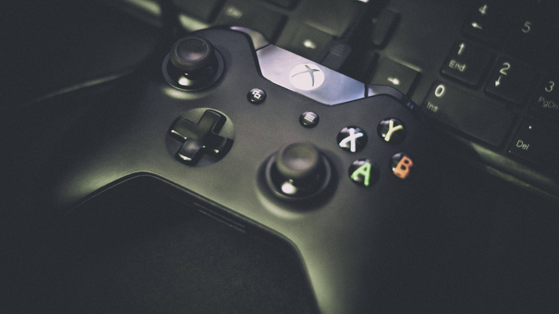 黑色Xbox手掣放在鍵盤上，按鈕在昏暗光線中發光。