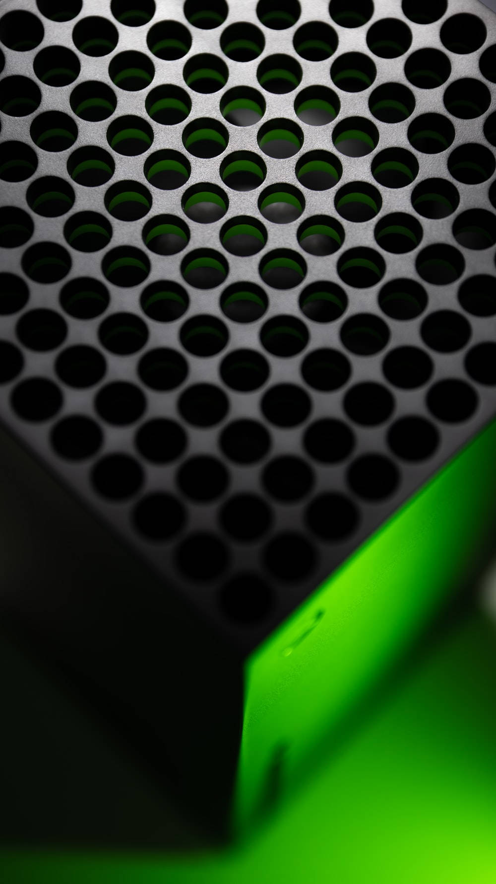 Xbox Series X 上方特寫 壁紙 — 黑色穿孔金屬表面的特寫，帶有發光的綠色光線，投射出銳利的陰影和高光。
