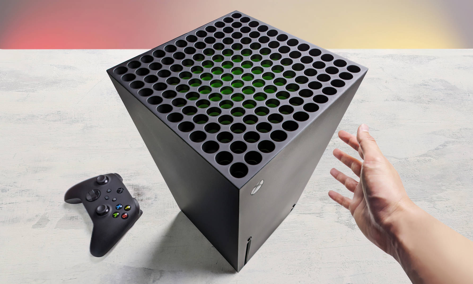 Xbox Series X 廣角照片 壁紙 — 一隻手伸向黑色Xbox Series X主機，內部發出綠色光芒，旁邊是其控制器，放在淺灰色表面上。