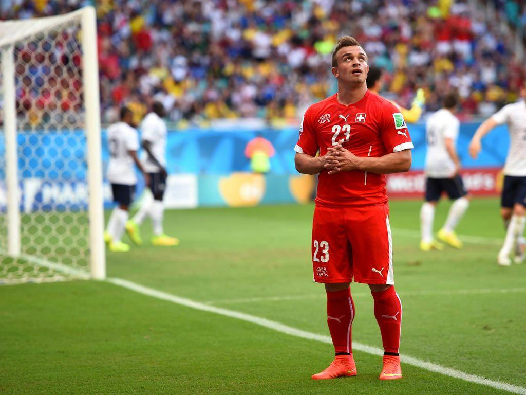 Xherdan Shaqiri 足球場致謝球迷 壁紙 — 一名身穿紅色球衣的瑞士足球員站在陽光明媚的綠色球場上，雙手合十，仰望上方，靠近球門柱。