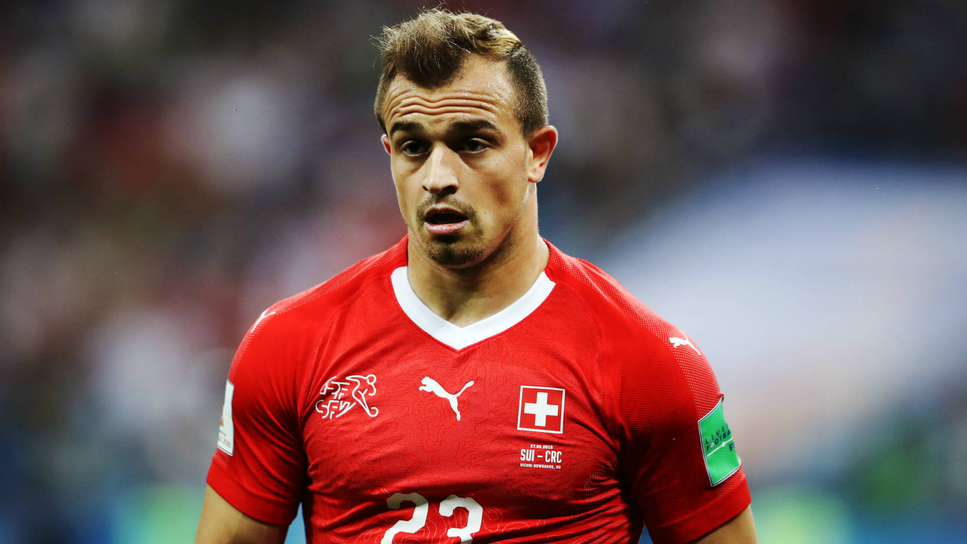 Xherdan Shaqiri 瑞士國家隊鬆一口氣 壁紙 — 一位專注的瑞士足球員，身穿紅色球衣，背號23，在比賽期間站在球場上。
