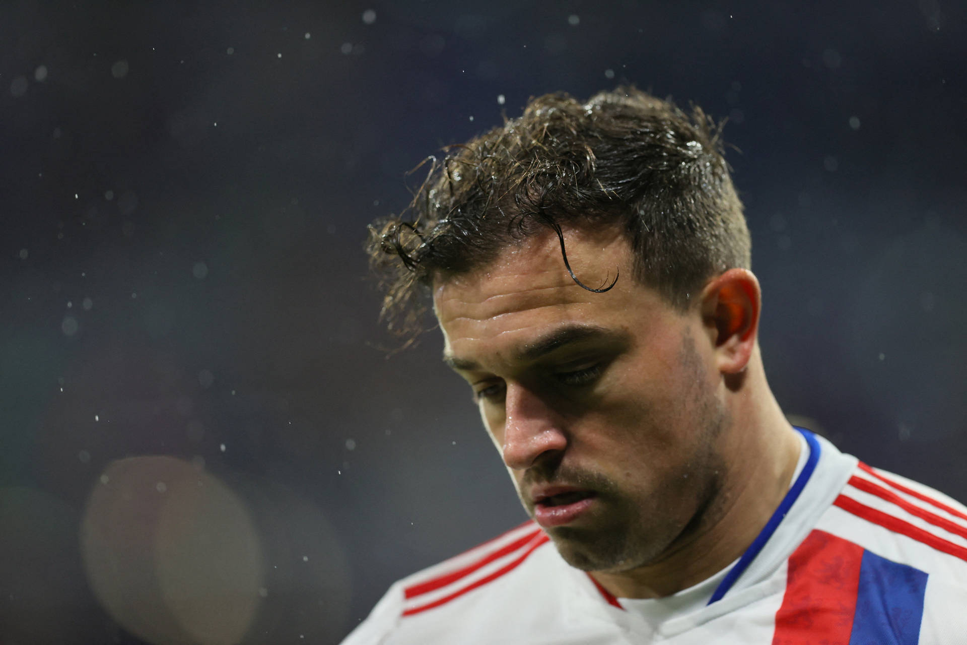 Xherdan Shaqiri 足球賽場失落瞬間 壁紙 — 特寫鏡頭：一名汗流浹背的足球運動員濕著頭髮低頭注視，背景是模糊的球場。
