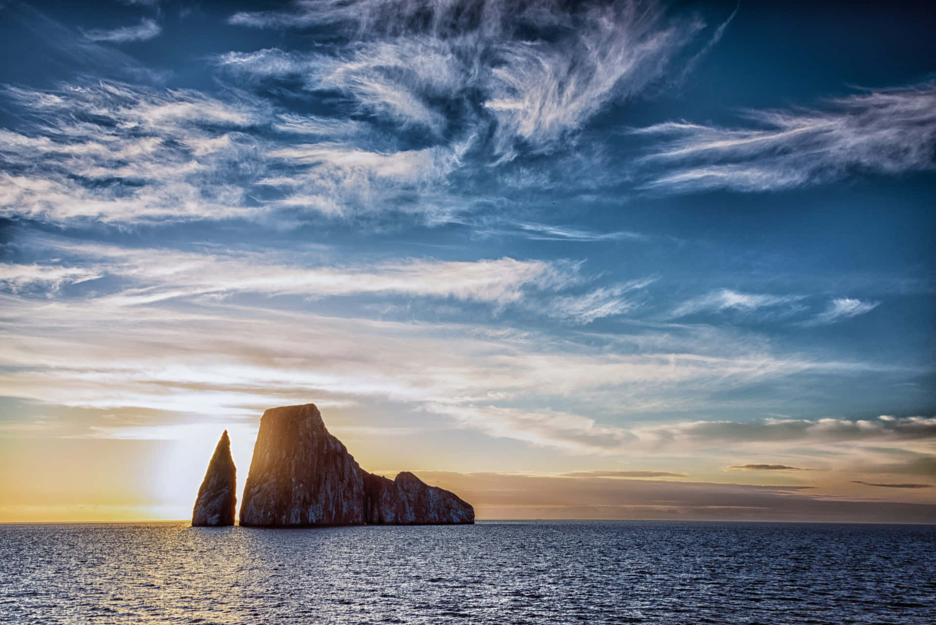  壁紙 — 夕陽將戲劇性的海蝕柱沐浴在金色光芒中，背景是廣闊的天空，點綴著縷縷薄雲。