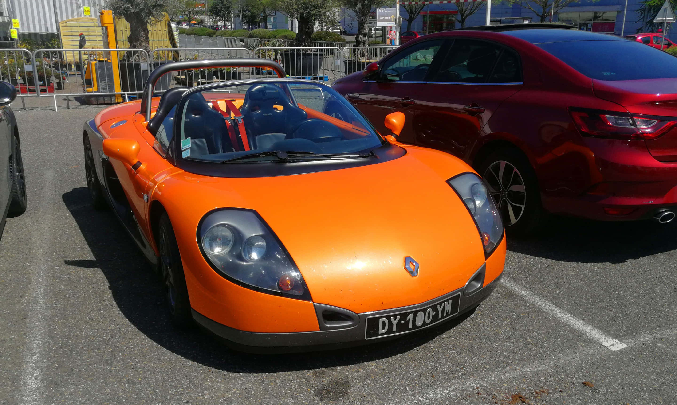 Renault Sport Spider 桌布 壁紙 — 一輛鮮橙色的雷諾Spider跑車在日間停泊在戶外停車場，旁邊有一輛紅色房車。