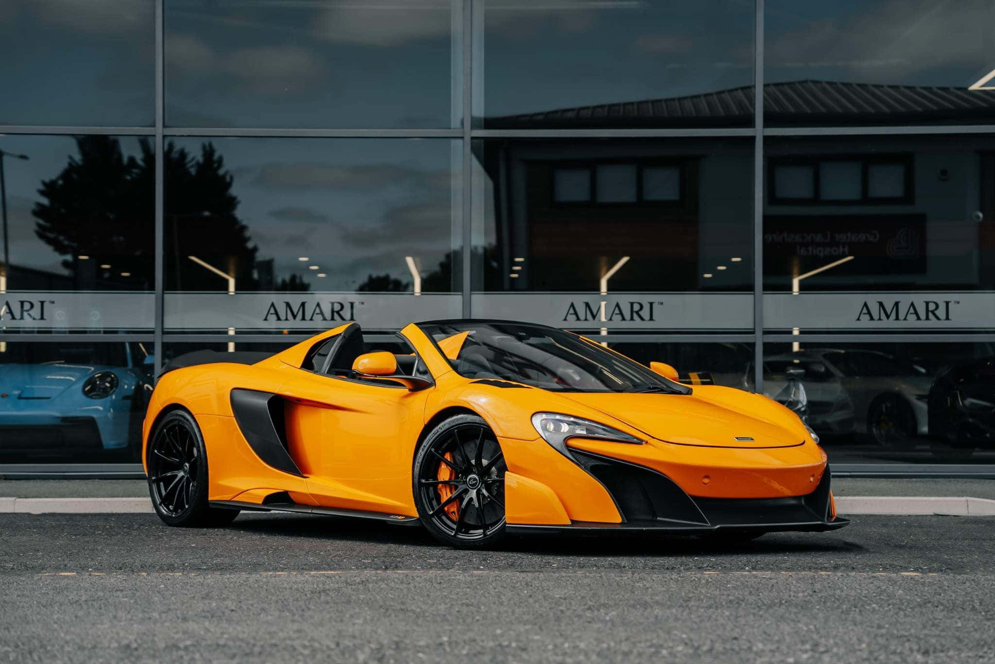 Mclaren 675lt Spider 桌布 壁紙 — 一輛鮮橙色的McLaren跑車在黃昏時停泊在玻璃幕牆的AMARI陳列室外。
