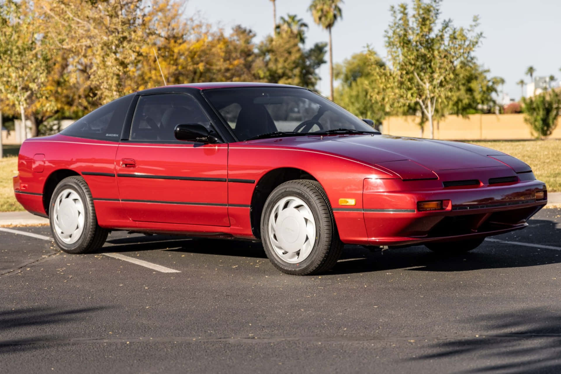  壁紙 — 一輛鮮紅色的1980年代日產300ZX跑車停泊在陽光充足的地方，背景有棕櫚樹和秋葉。