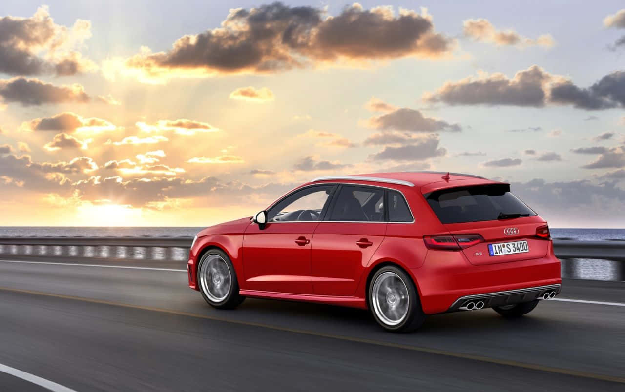 Audi S3 桌布 壁紙 — 一輛鮮紅色的Audi旅行車在金色雲彩的戲劇性日落天空下，沿著海岸高速公路行駛。