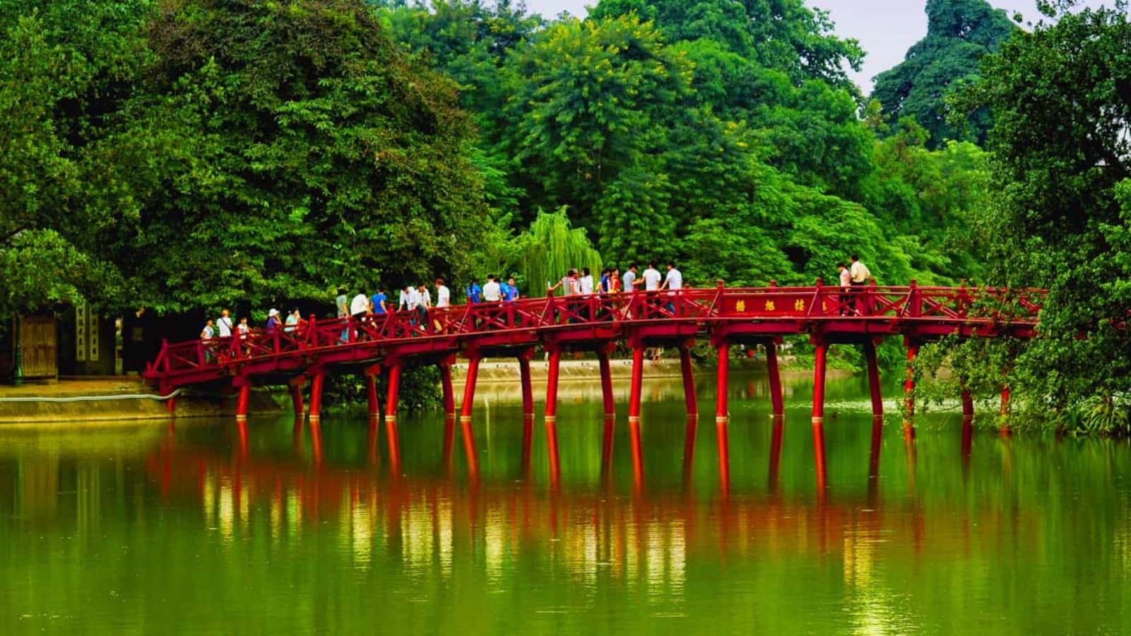 綠色池塘上的紅色木橋，有行人走過和樹木